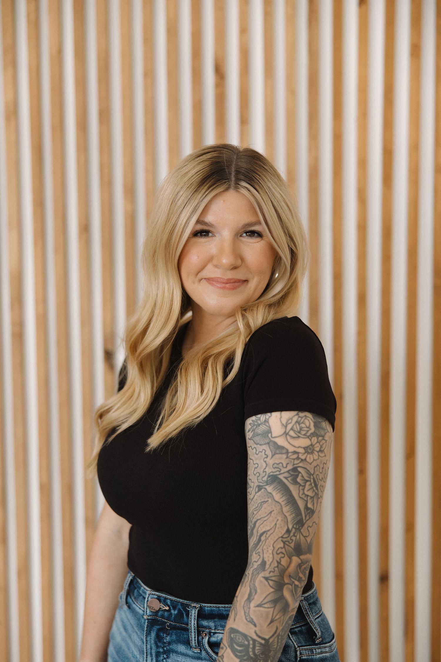 Portrait against wooden slat wall showing casual style and tattoo art.