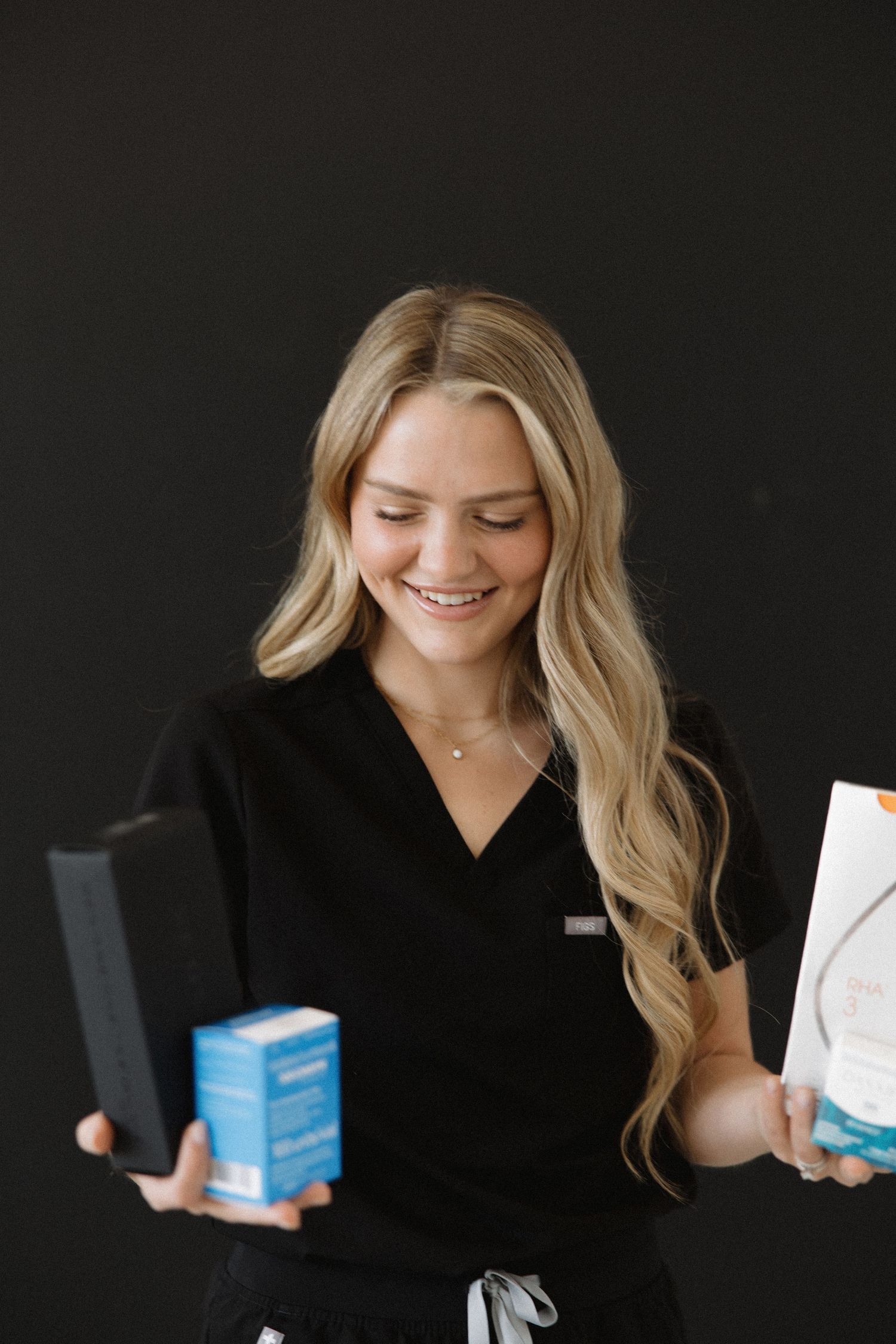 Person in black holding medical product boxes against dark background.