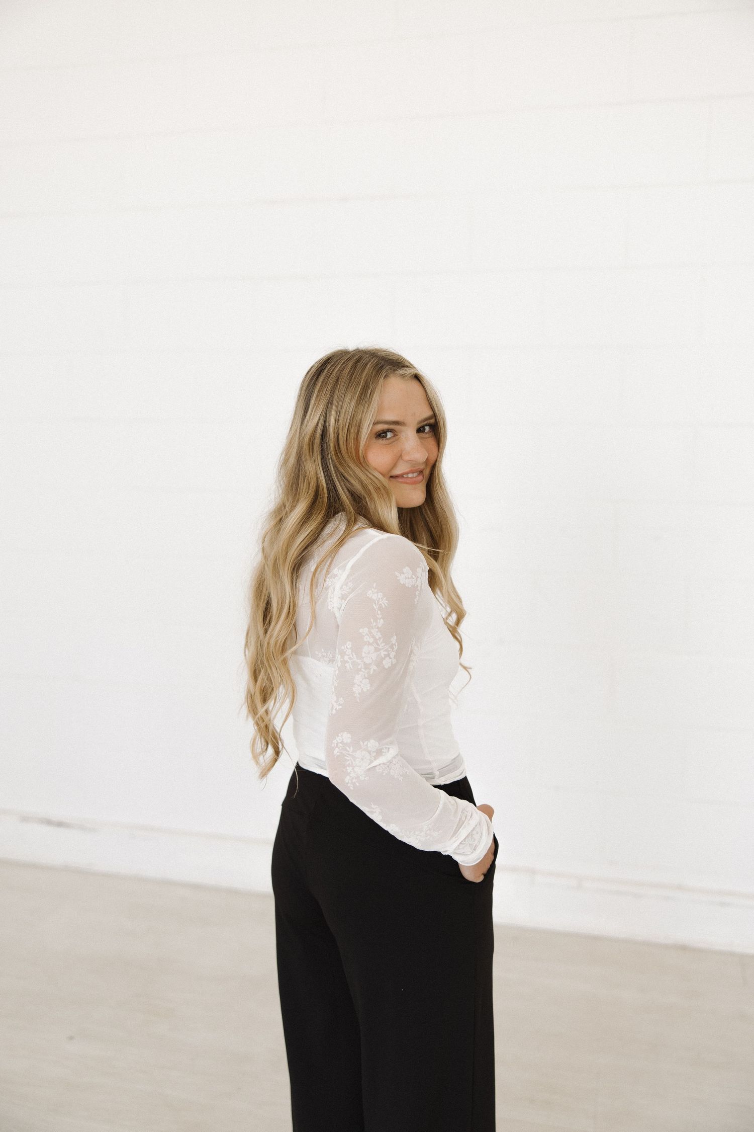 Woman in monochrome outfit poses playfully in minimalist studio setting.