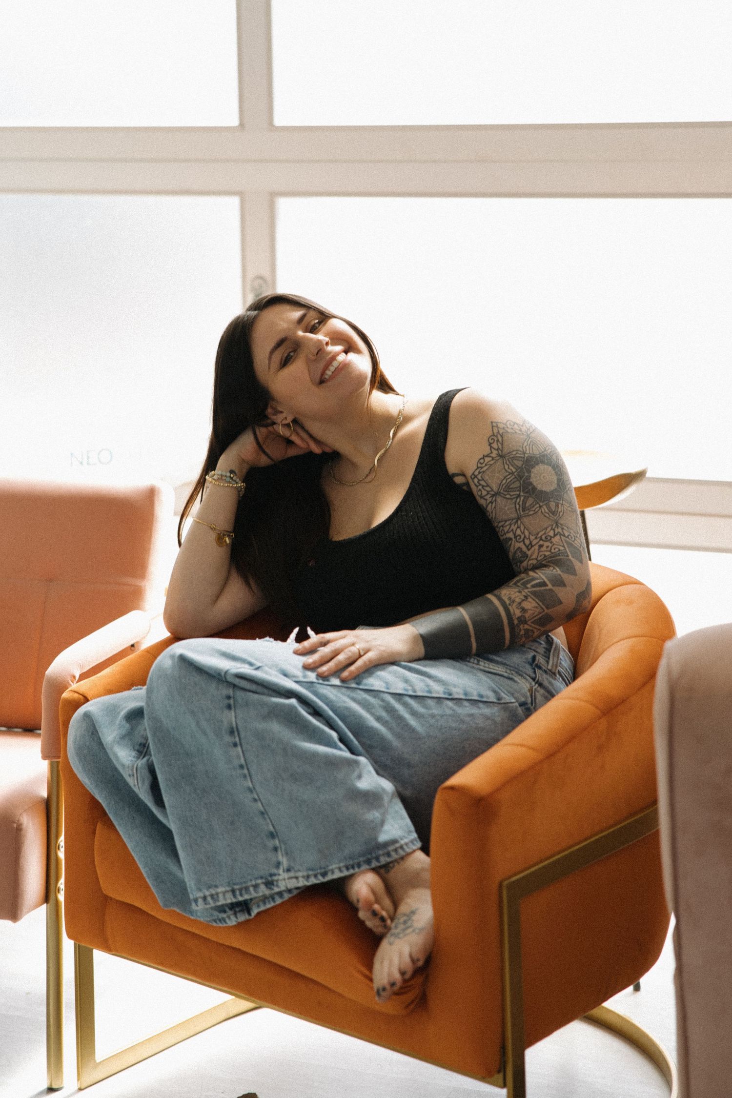 Relaxed pose on an orange armchair wearing denim and casual attire.