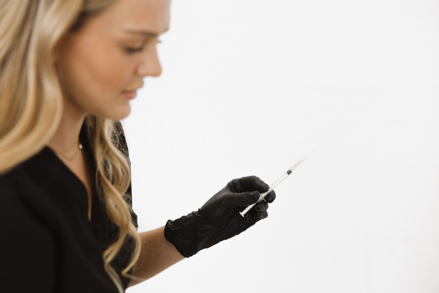 Closeup of cosmetic procedure being performed with black gloves and white background.