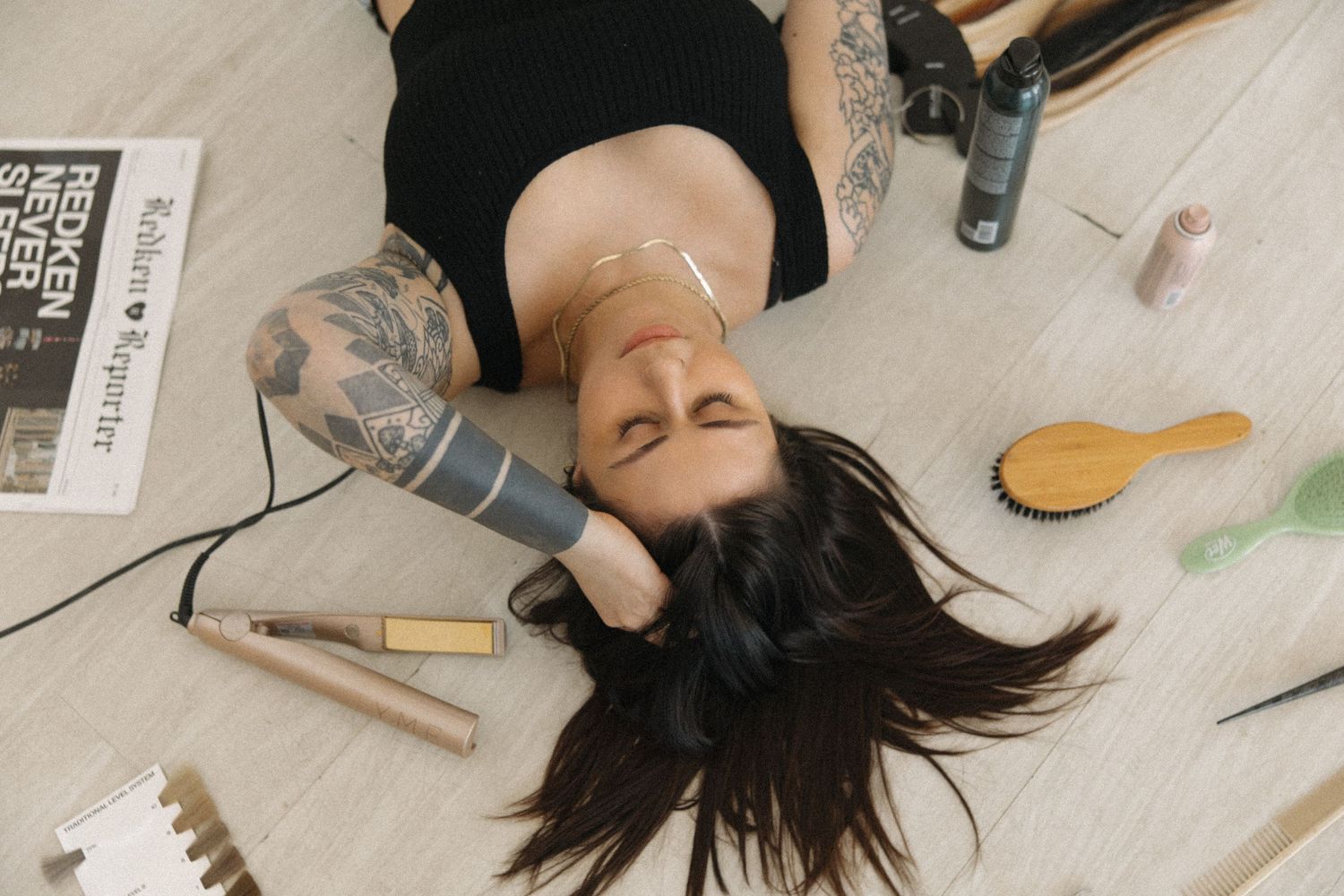 Artistic photo of person reclining on floor with hair care tools and beauty products arranged around.