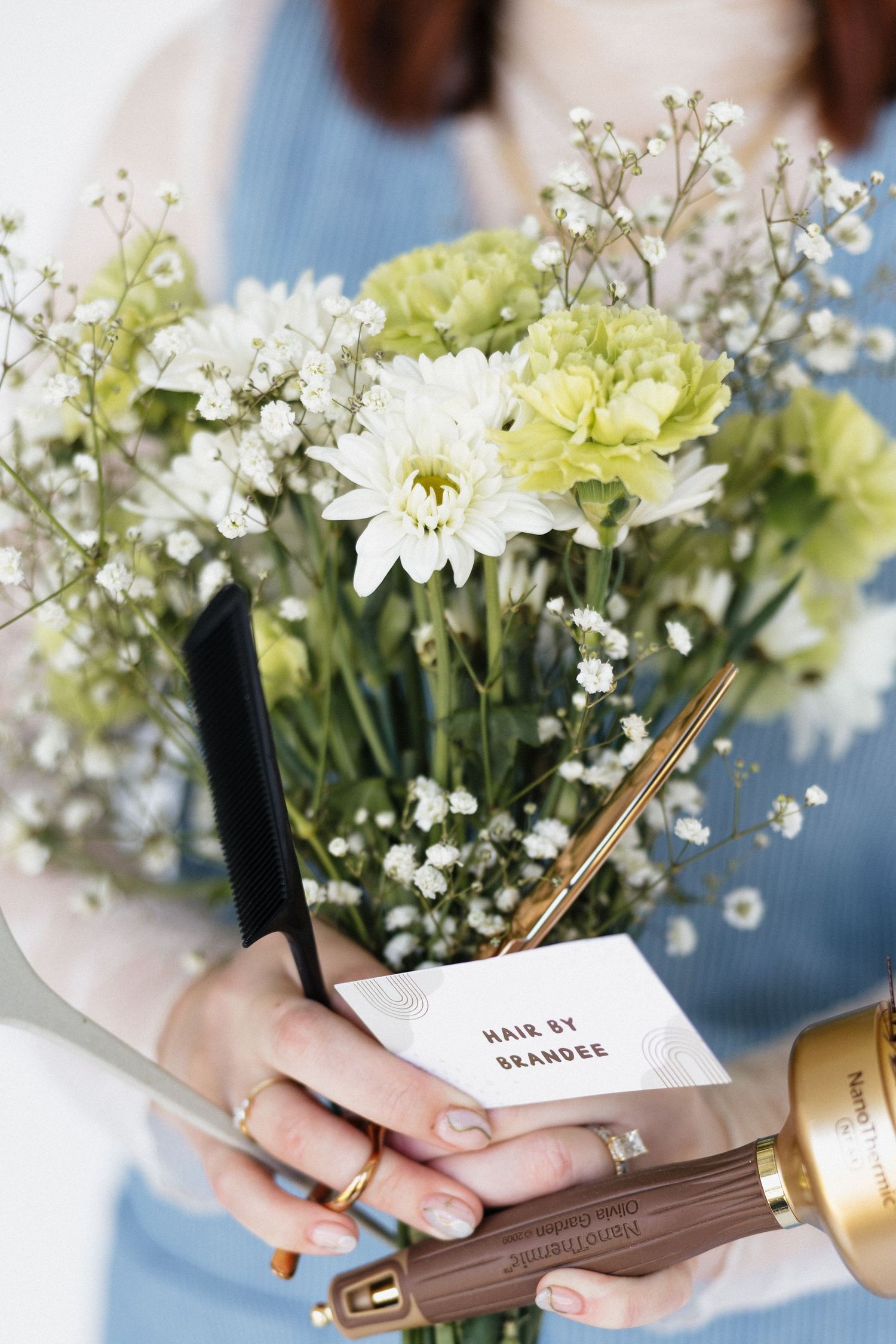 A delicate arrangement of daisies and baby's breath with styling tools and a note card.