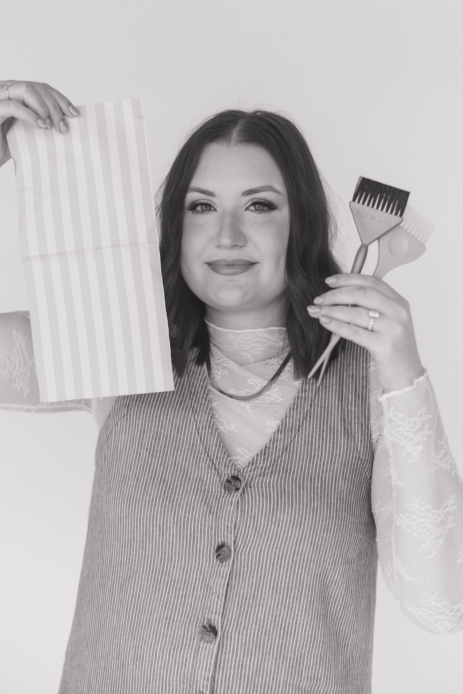 Professional holding hairstyling tools while wearing a striped cardigan and white lace sleeves.