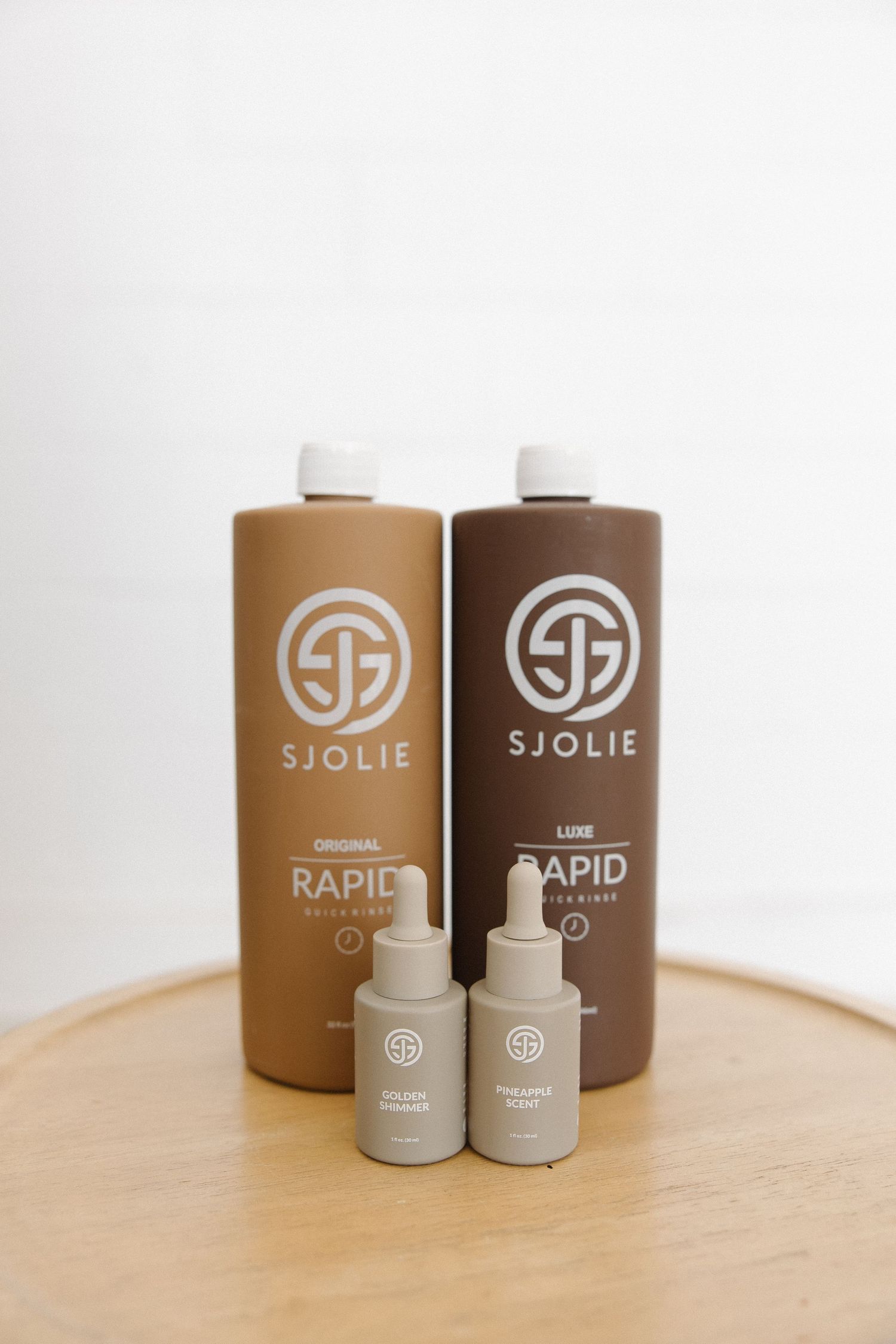 Two brown bottles and two small dropper bottles of Sjolie brand products displayed on wooden surface.