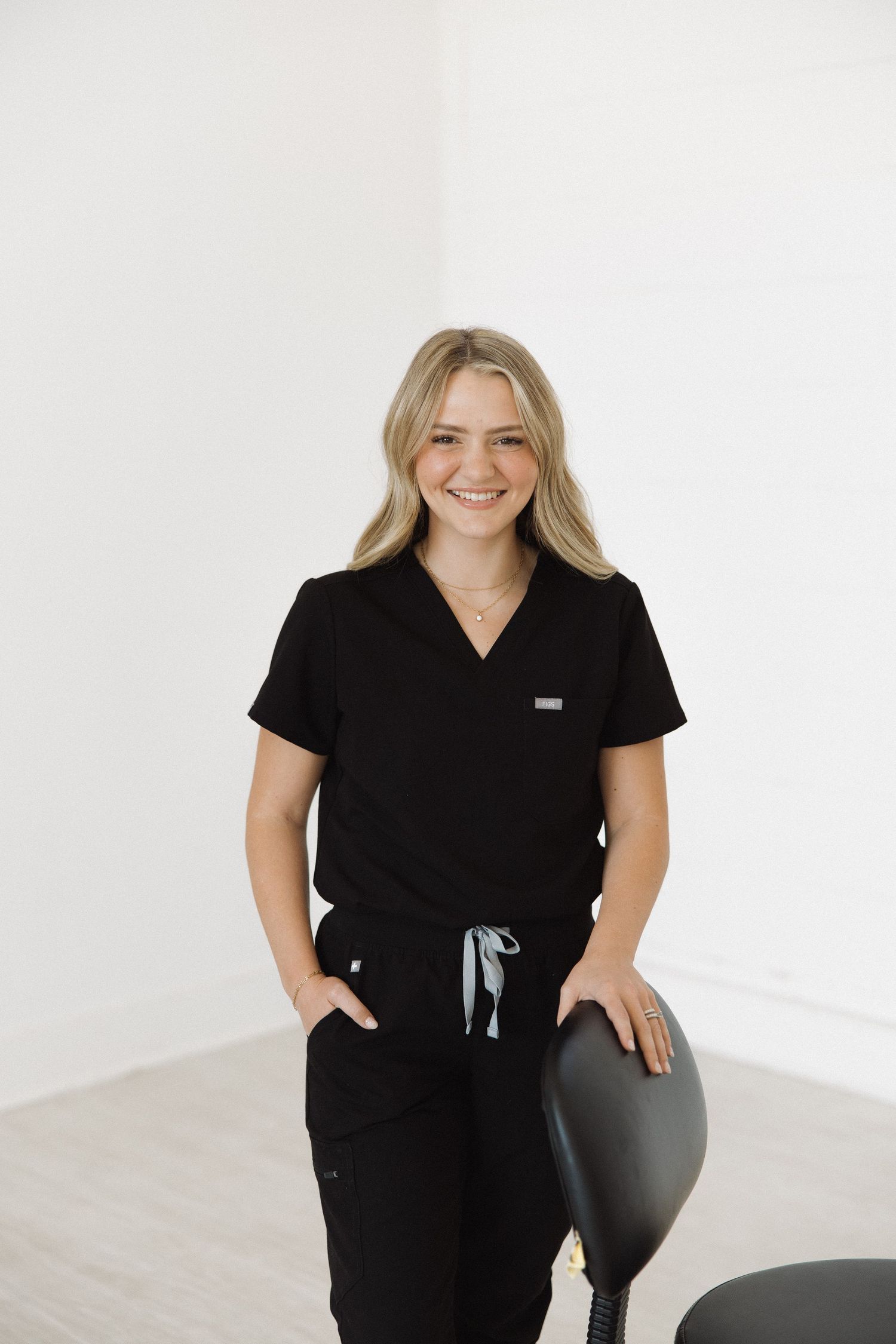 Medical professional in black uniform stands casually next to office chair in bright room.