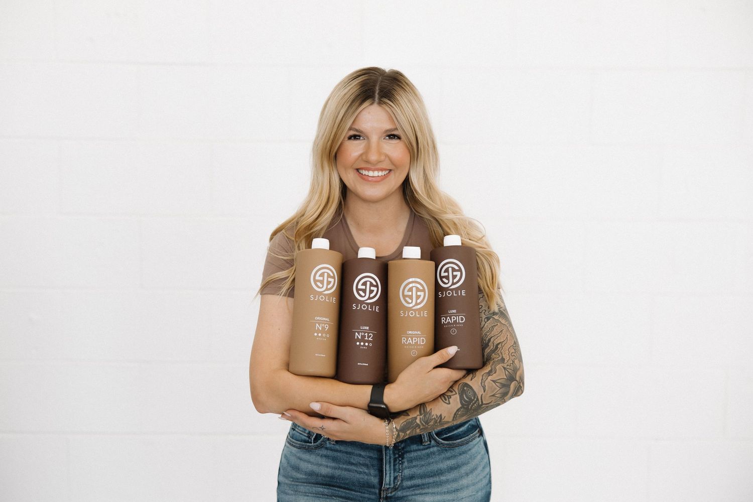 Product shot featuring multiple SJOLIE tanning solution bottles in neutral brown tones.