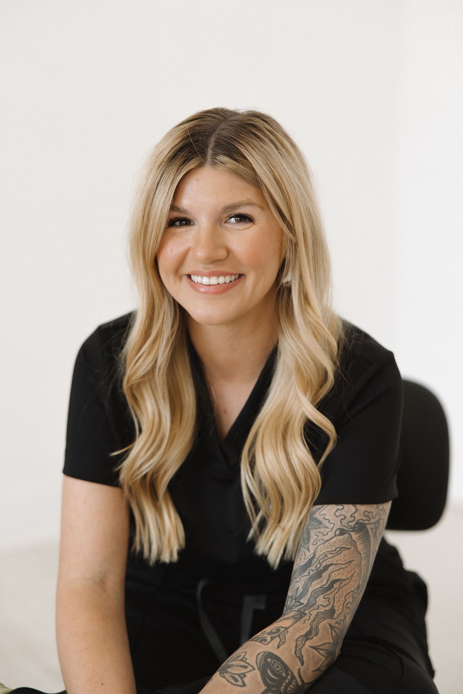 Professional studio portrait of a person with blonde hair wearing black clothing and showing tattoos.