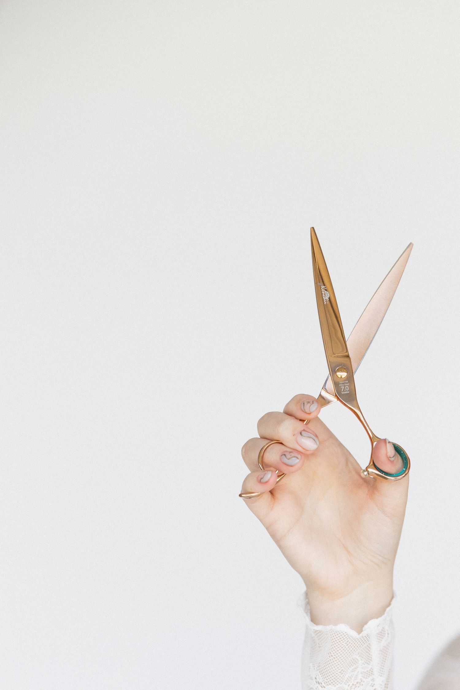 Hands holding gold scissors against white background in artistic composition.
