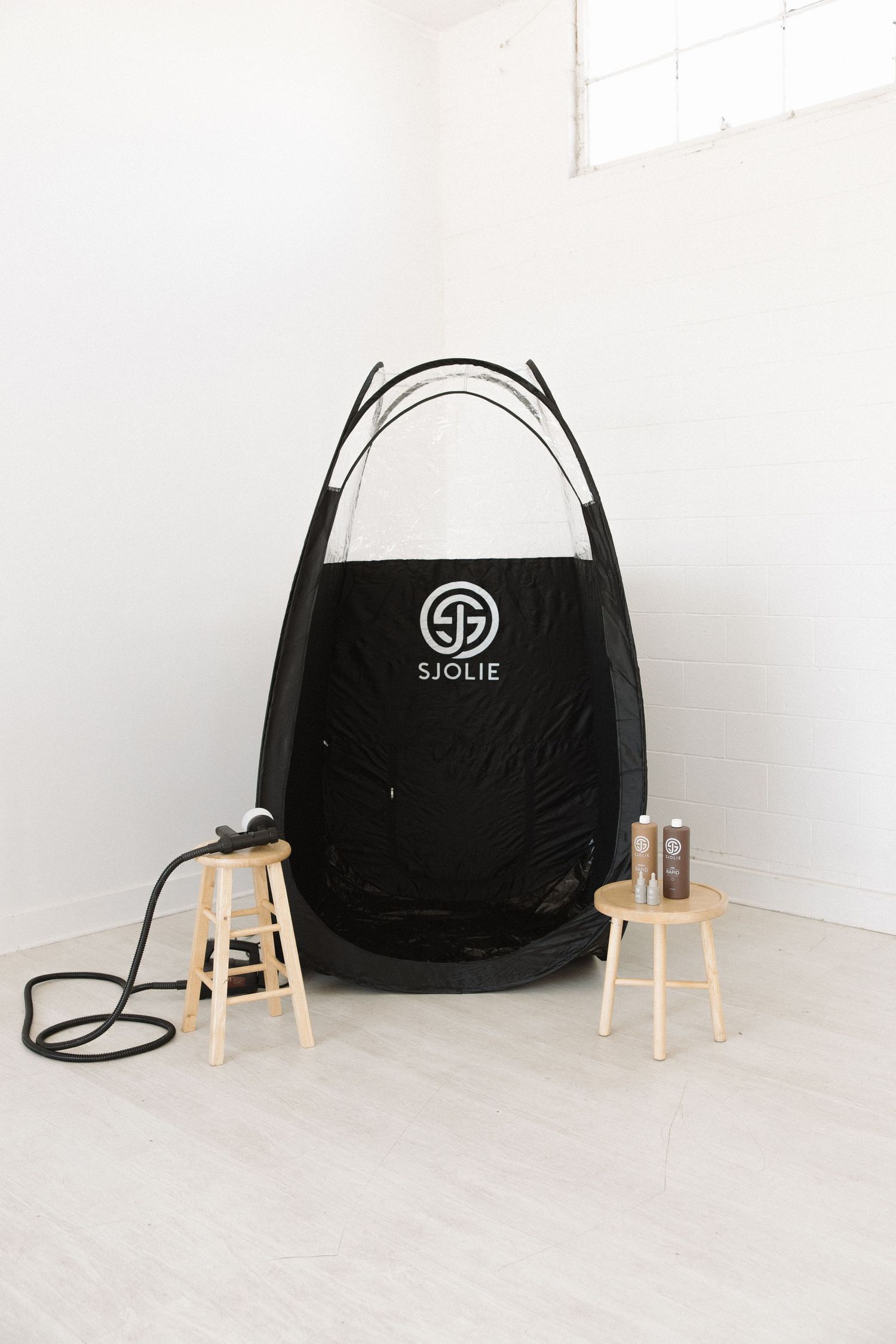 Professional spray tanning tent setup with Sjolie logo in minimal white room.