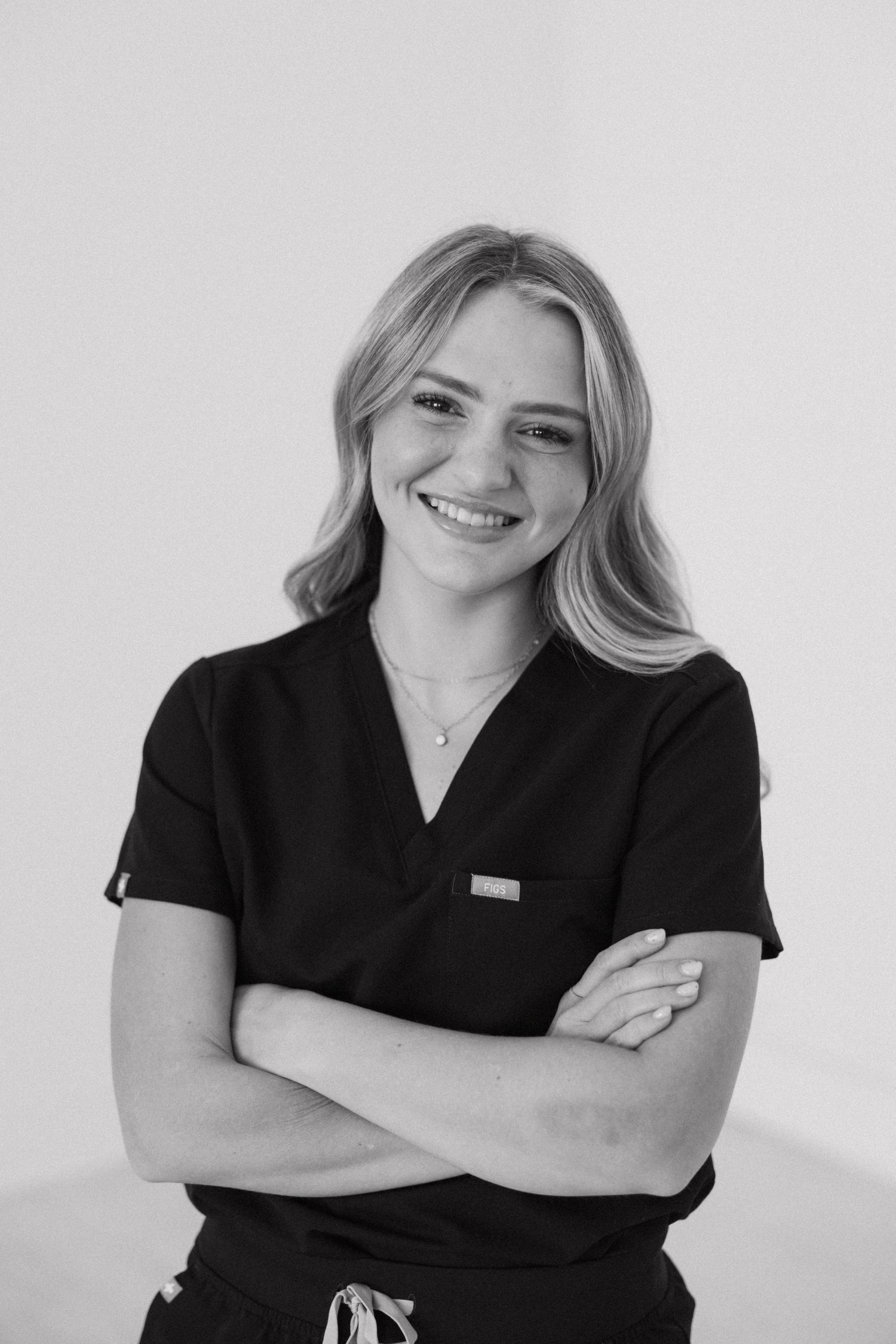 Healthcare professional in black scrubs poses confidently with crossed arms against white background.