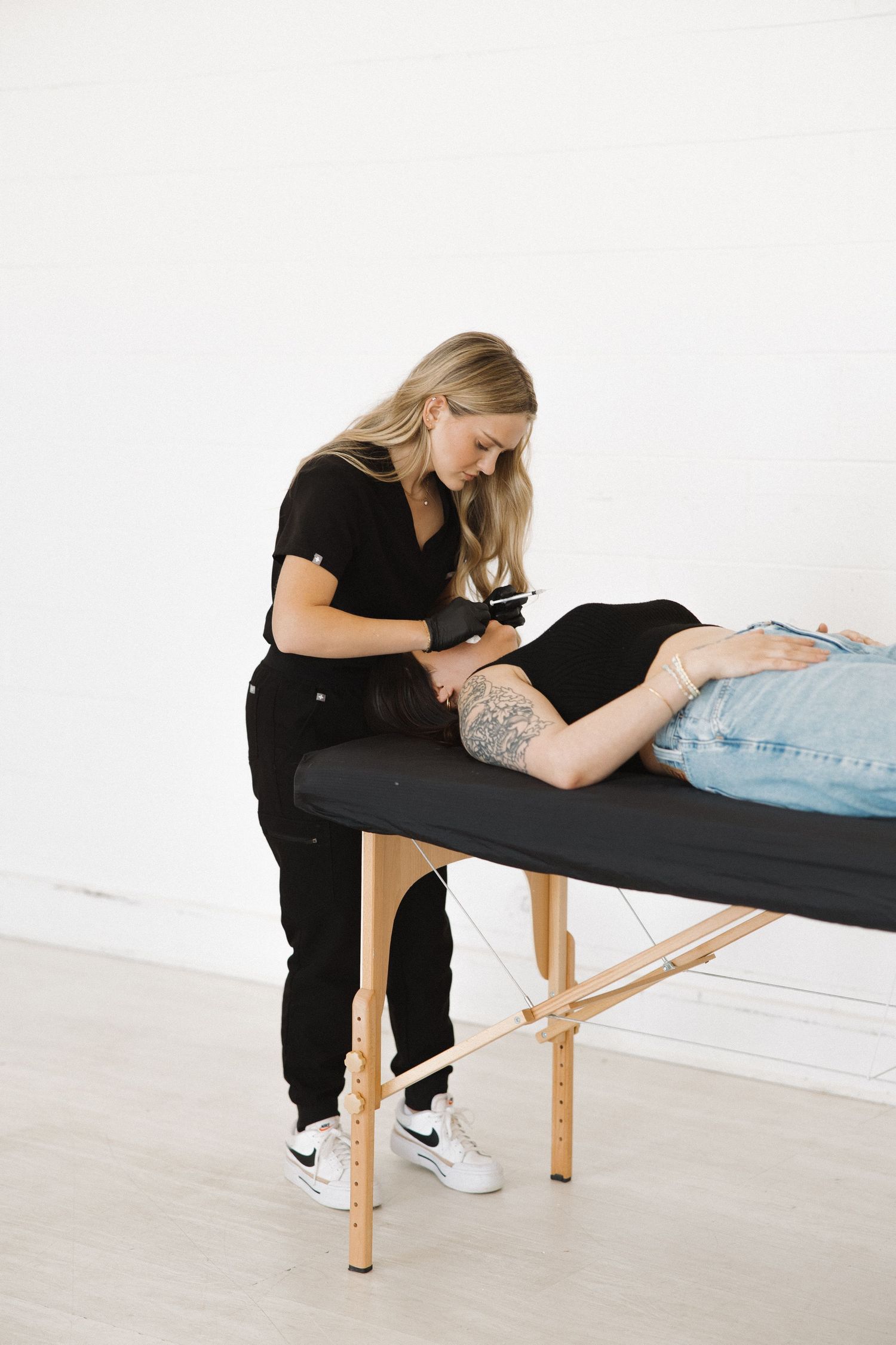 Beauty specialist working on client lying on treatment table in white studio.