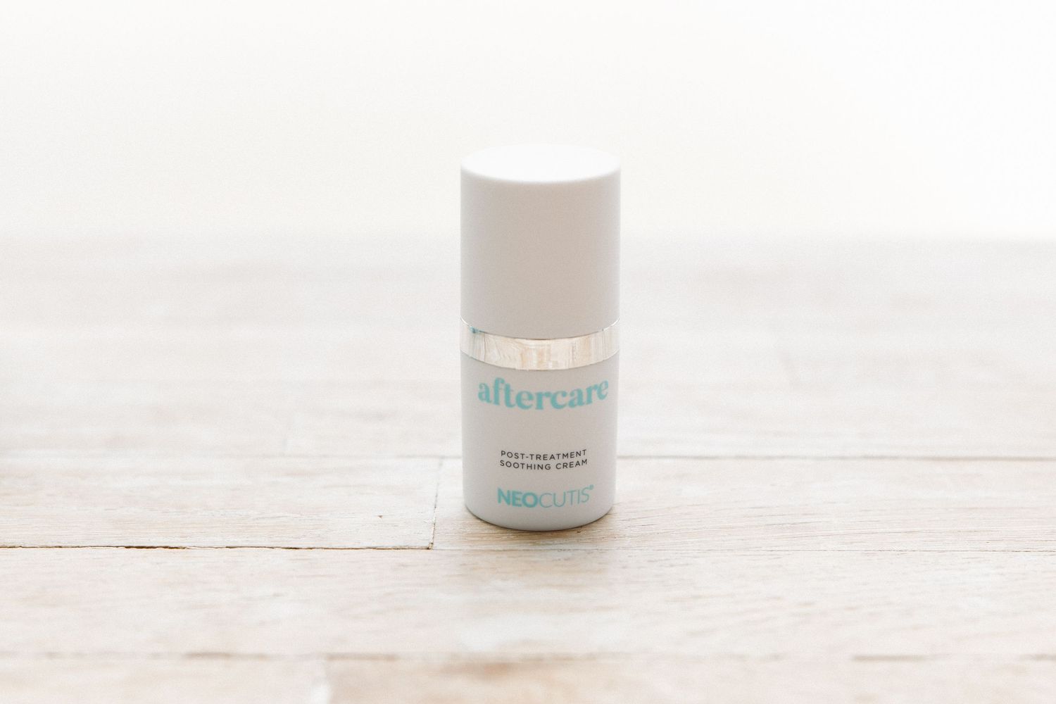 A white beauty product container with turquoise text on a light wooden surface.