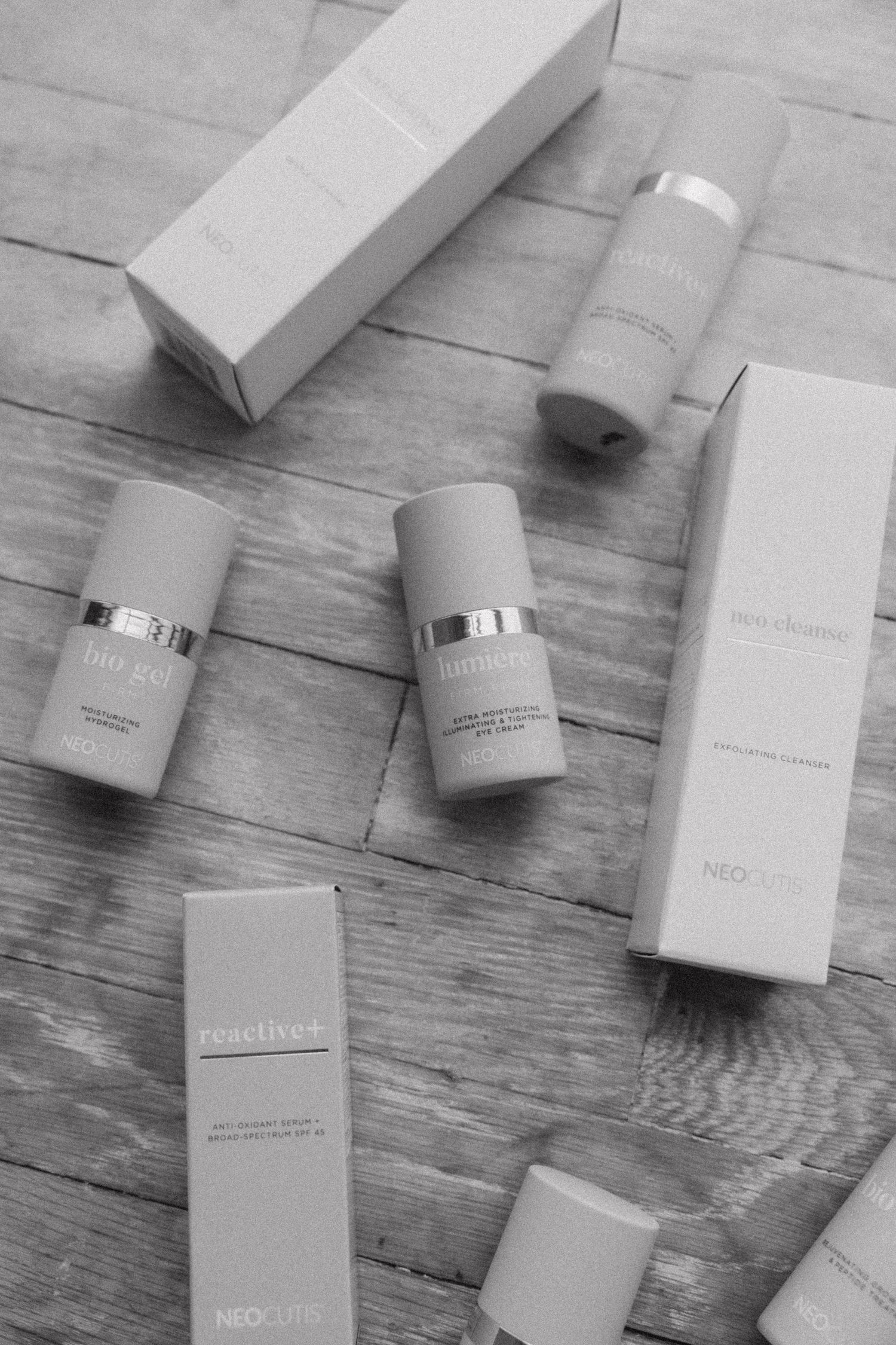 Beauty product containers in monochromatic tones arranged on rustic wooden surface.