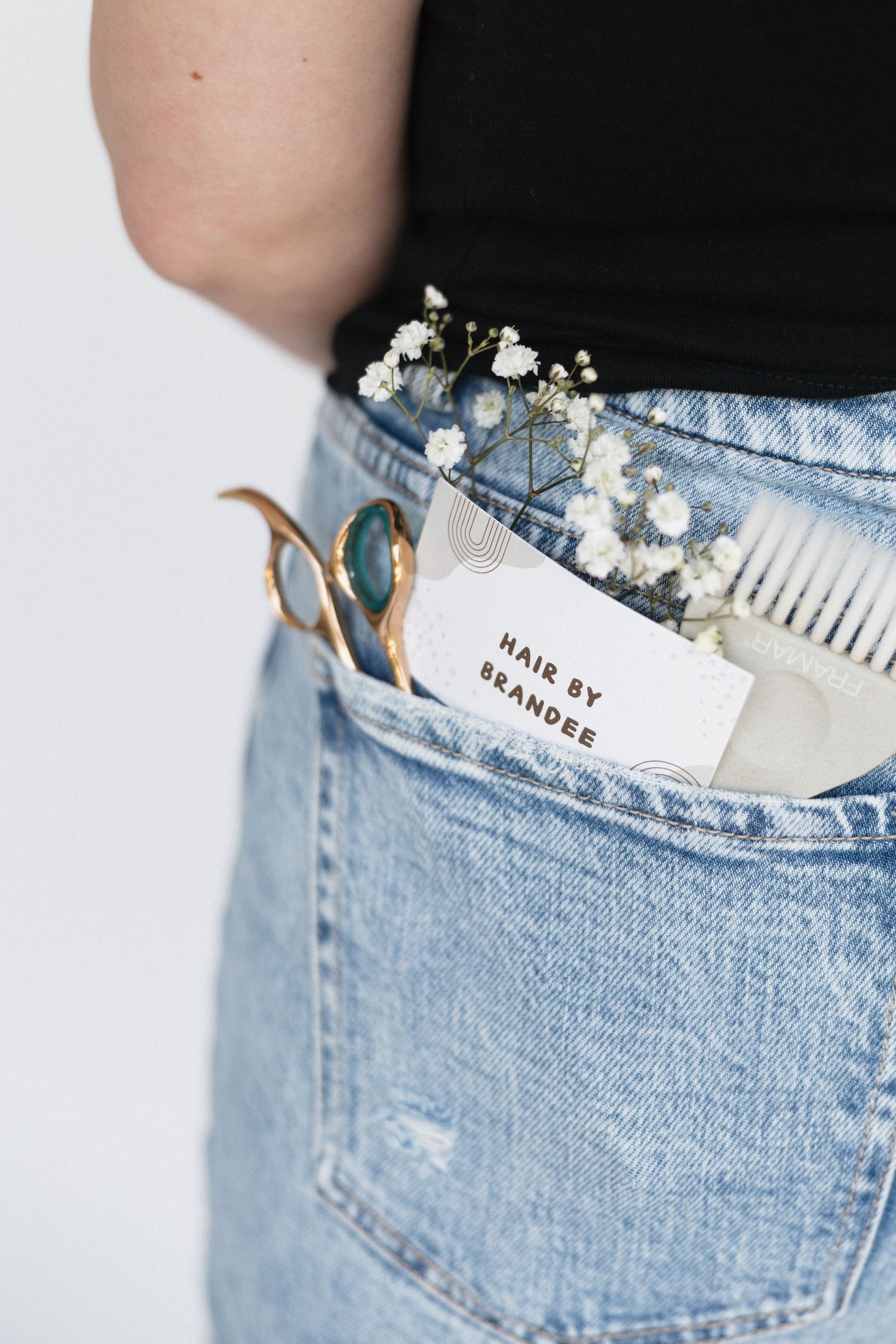 Close-up of hair styling tools and baby's breath flowers in denim jean pocket.
