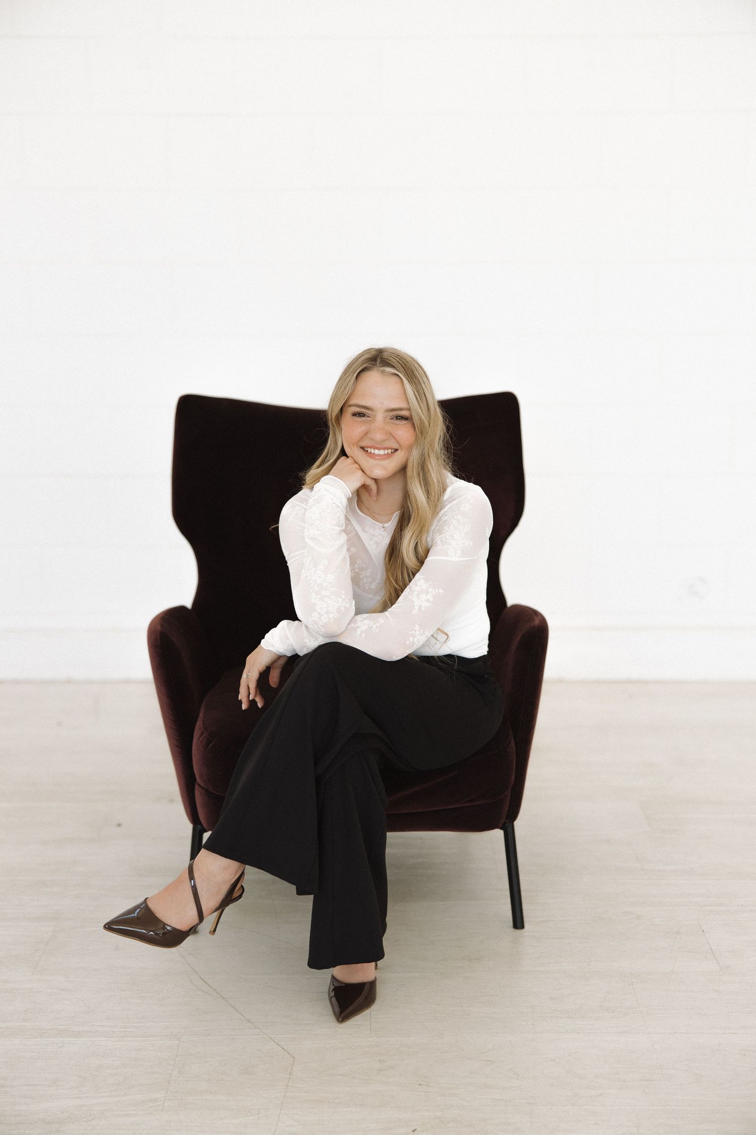 Modern studio portrait with subject lounging casually in dark velvet armchair wearing business casual attire.