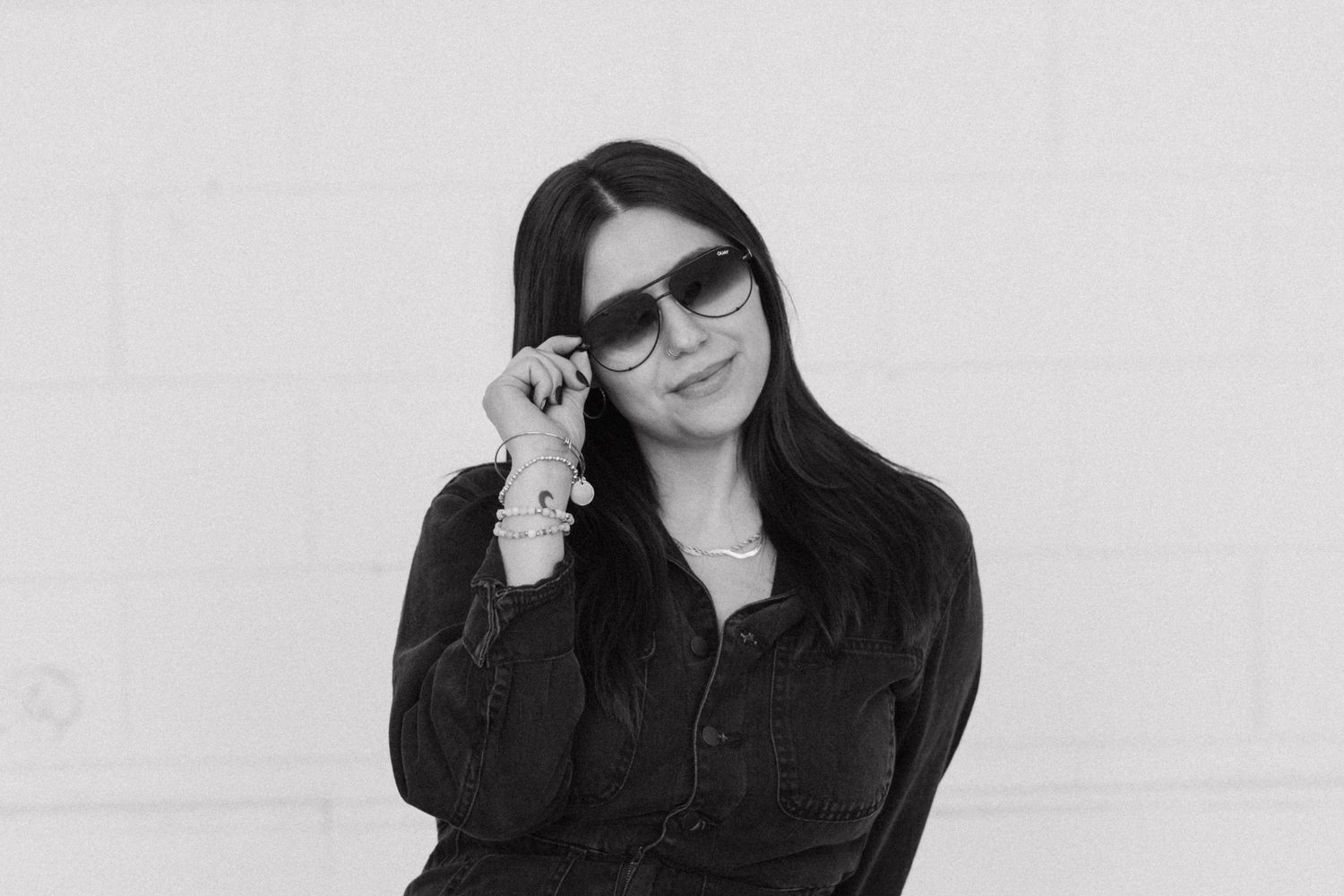 Figure with brown hair in black wearing sunglasses against white background.