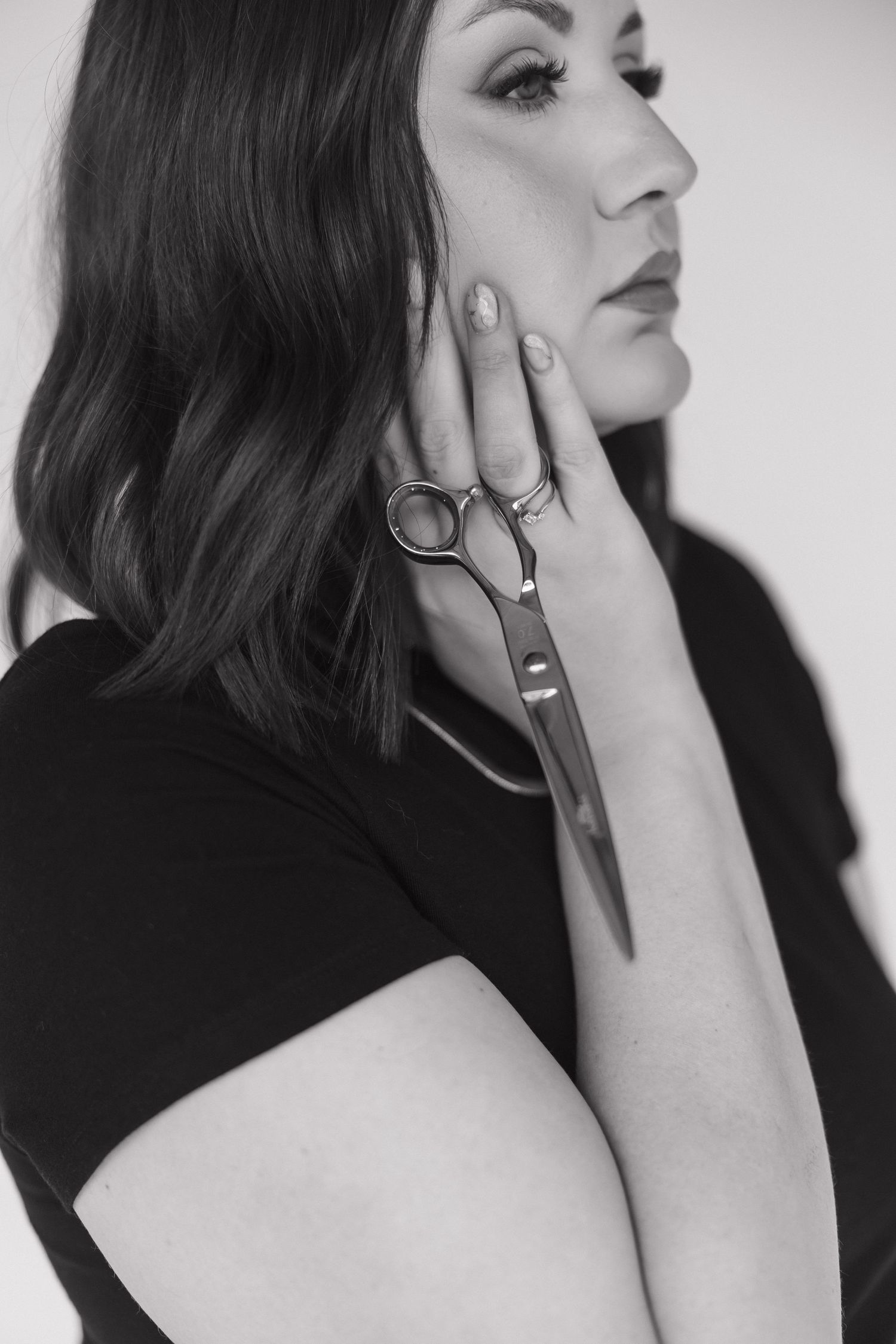 Artistic black and white portrait showing styling scissors held against face.