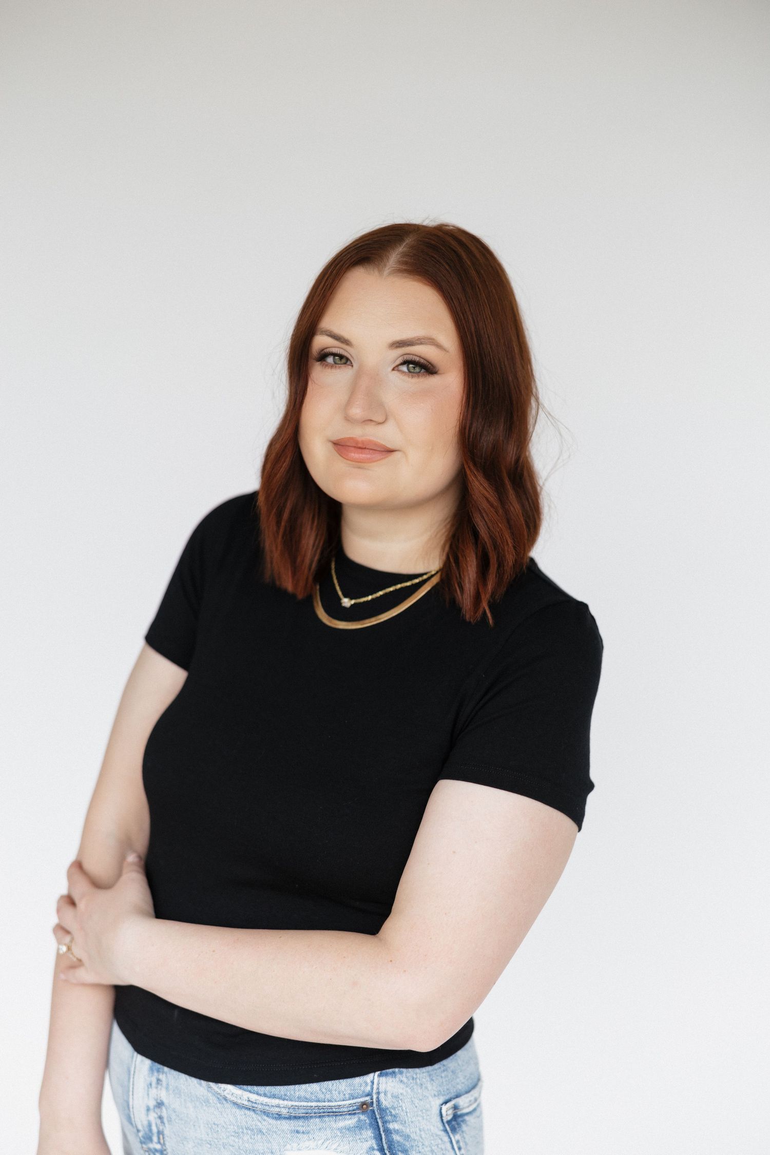 A casual hairstylist studio portrait featuring a black t-shirt and light denim jeans against a white backdrop.