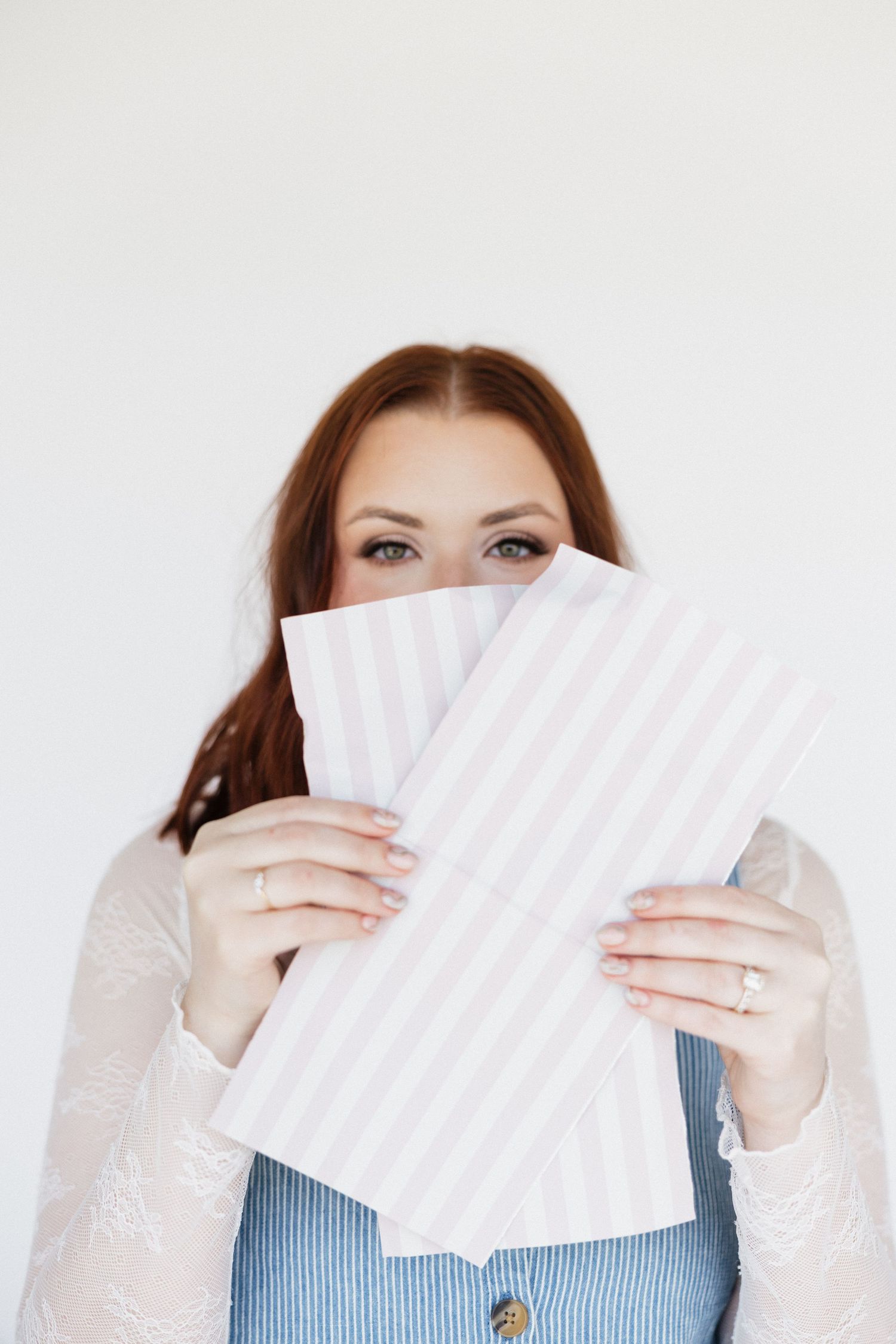 A person playfully hiding behind a pink and white striped hair foils against white background.