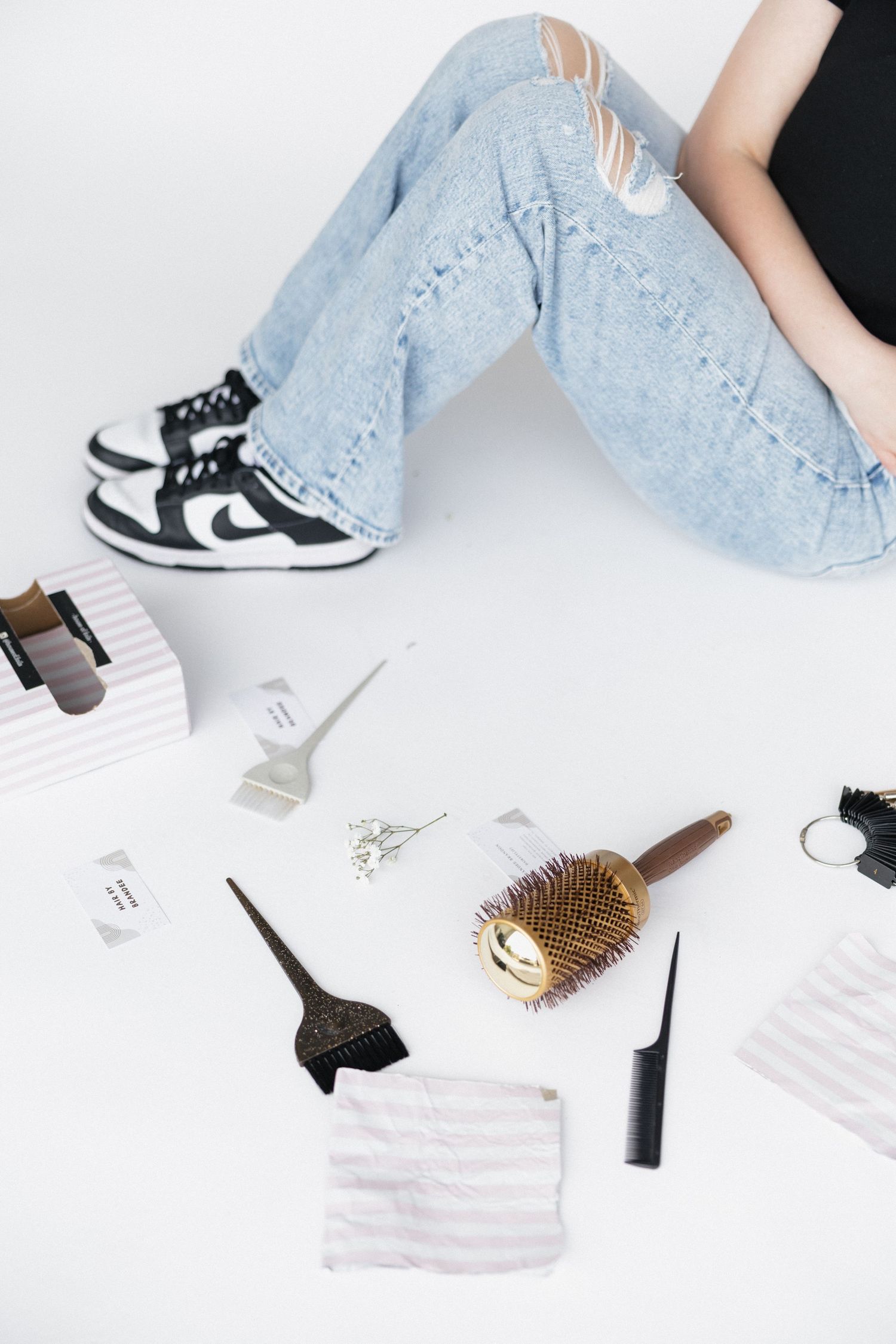 Beauty styling tools and products arranged on white background with black and white sneakers.