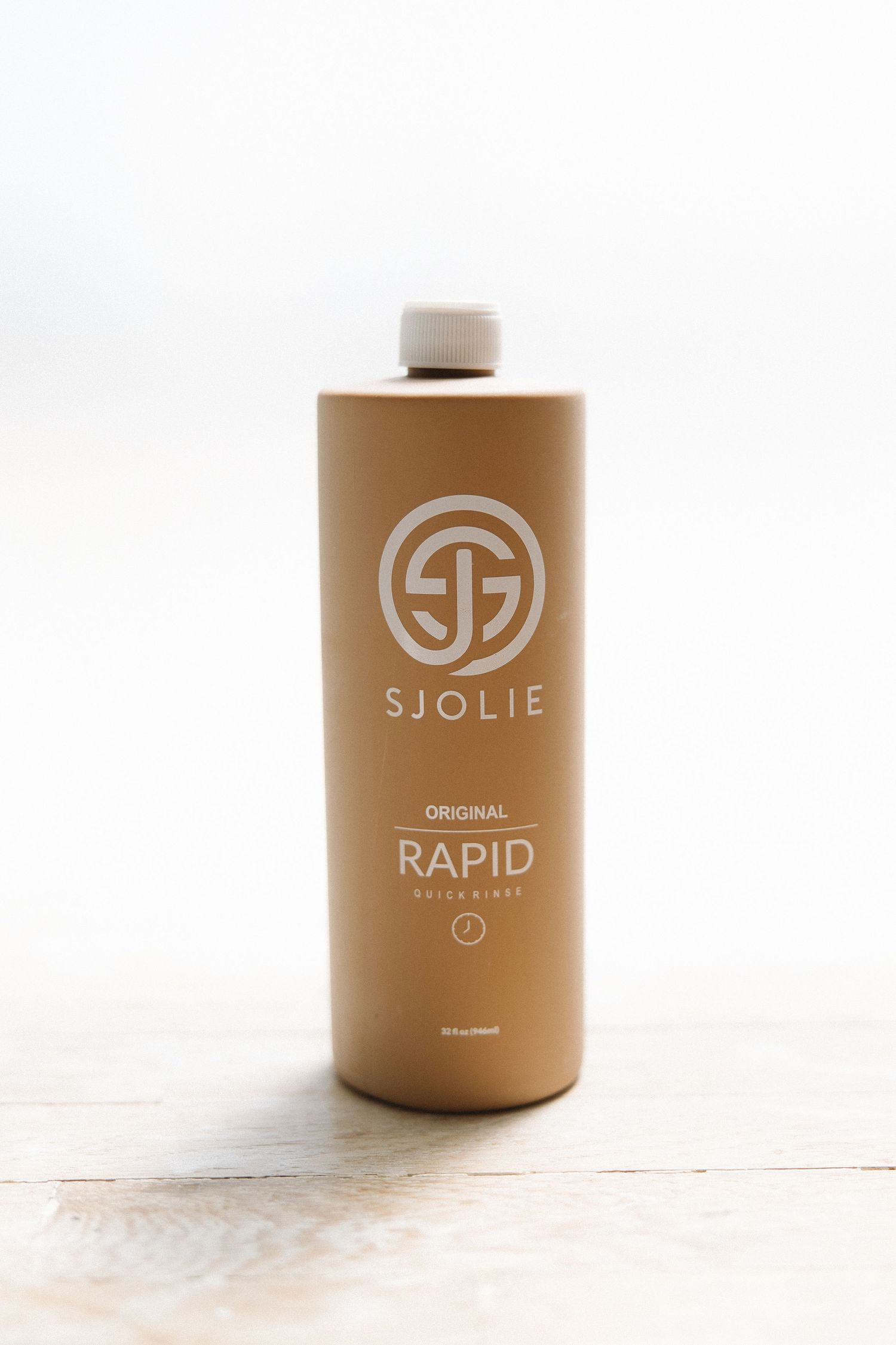 Large brown bottle of SJOLIE Original Rapid tanning solution on white wooden surface.