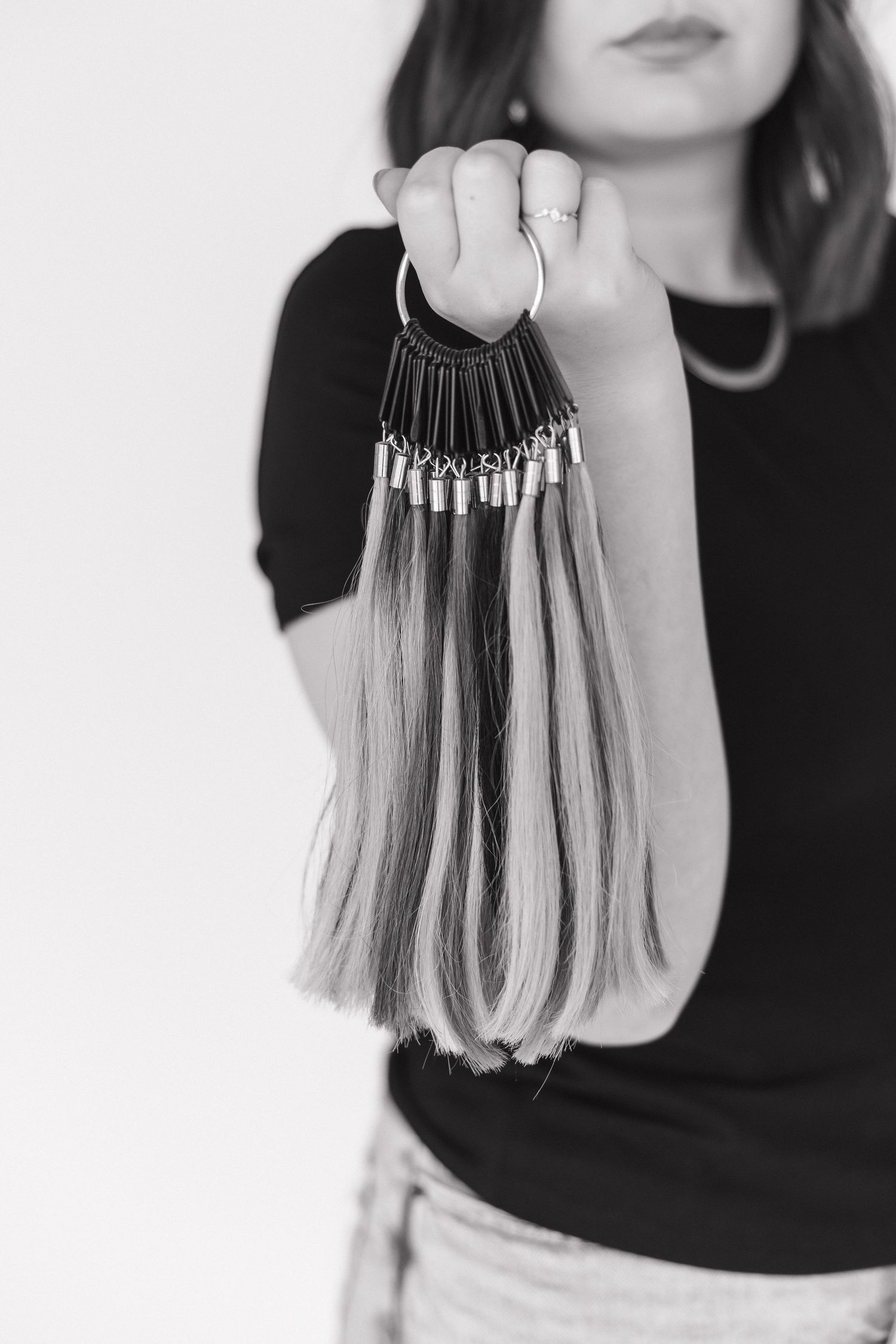 Hand holding color-matched hair extensions on a black display ring.