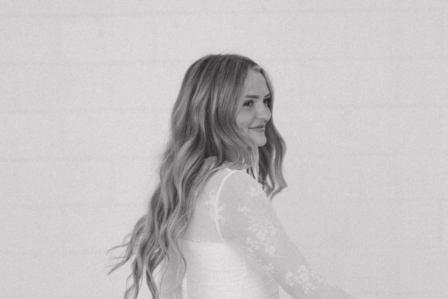 Woman in elegant white top poses against minimalist background.