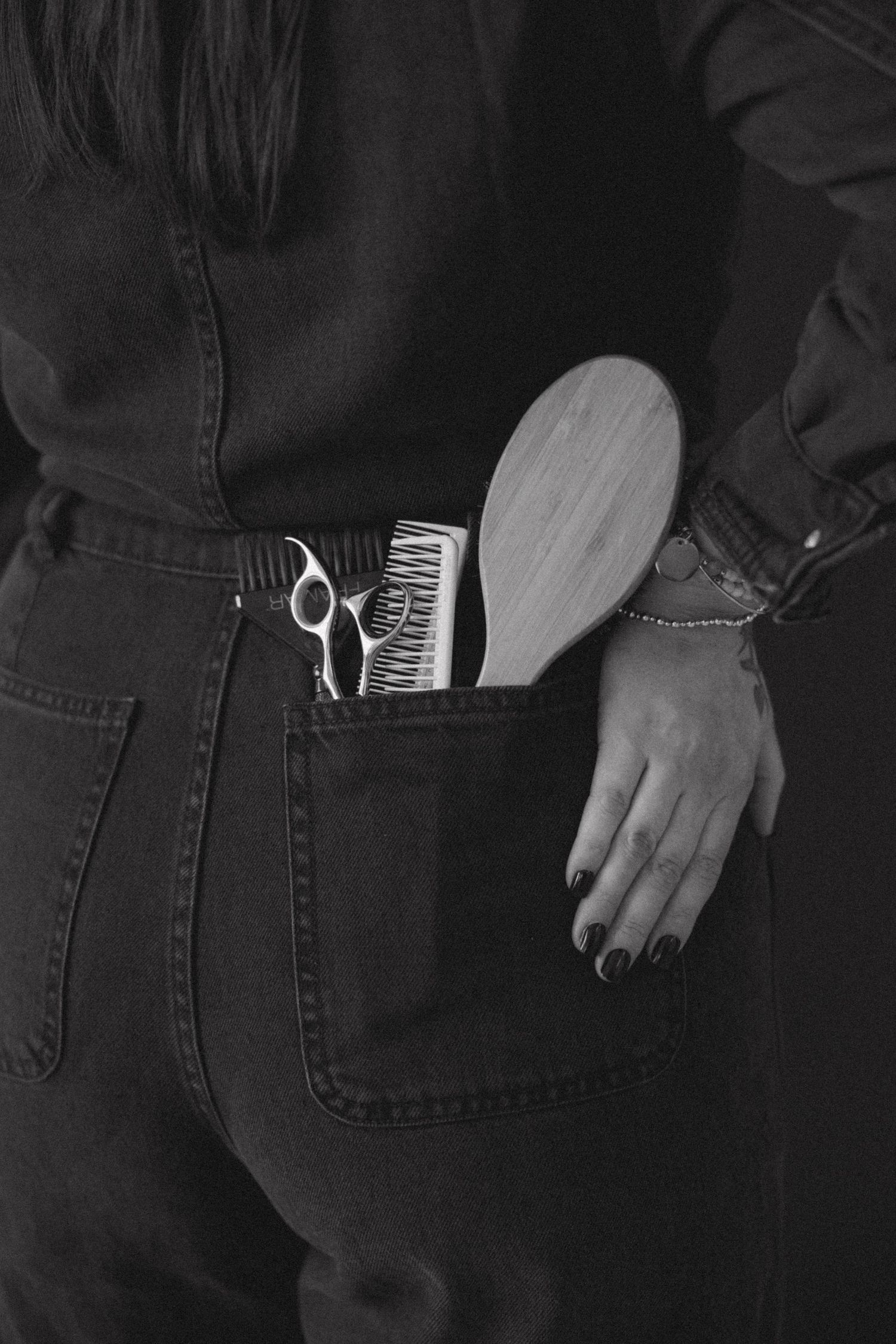 Hair styling tools tucked into back pocket of dark denim jeans.