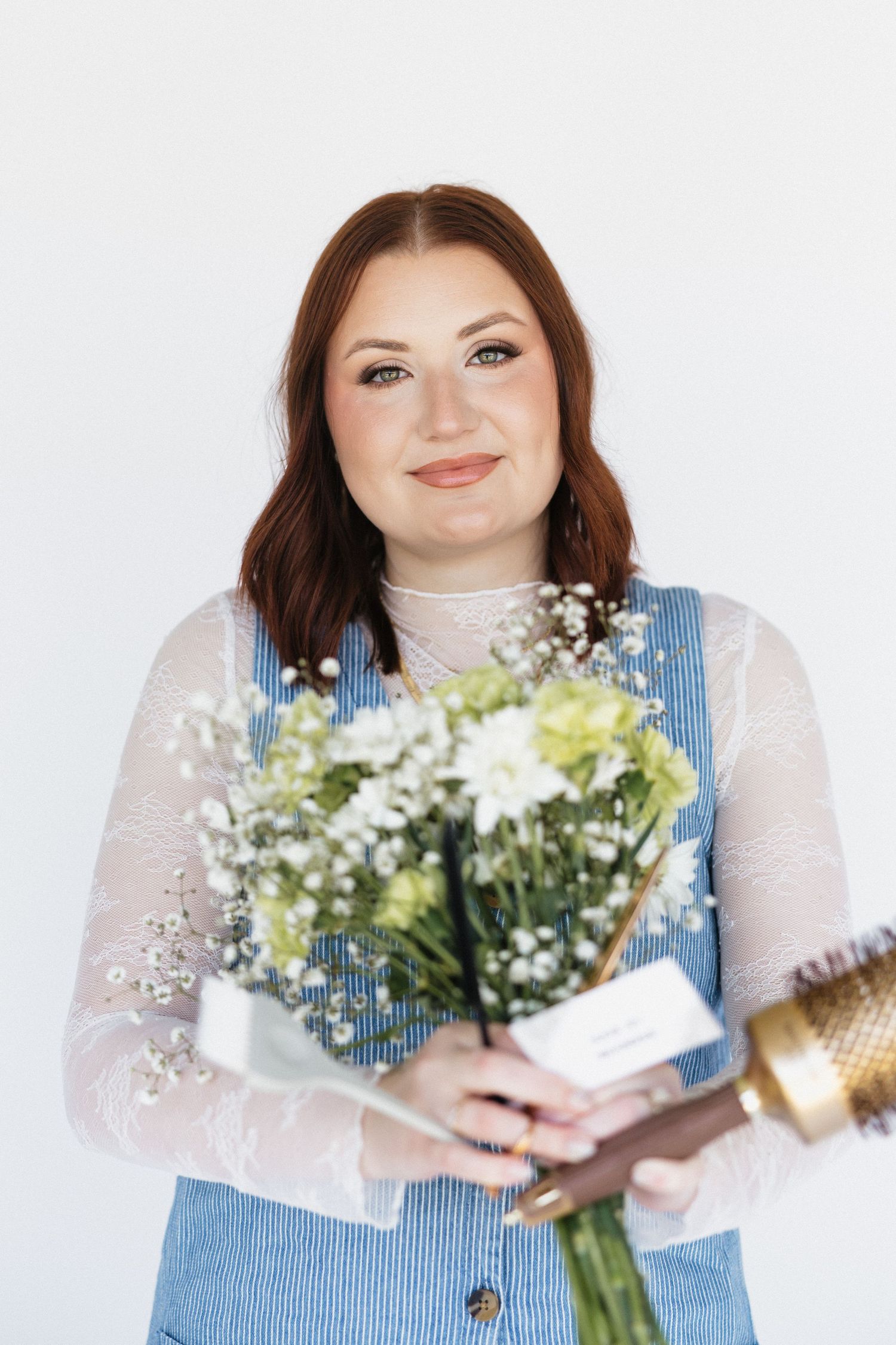 A person in a blue denim vest and white sheer top holds a fresh bouquet of flowers.