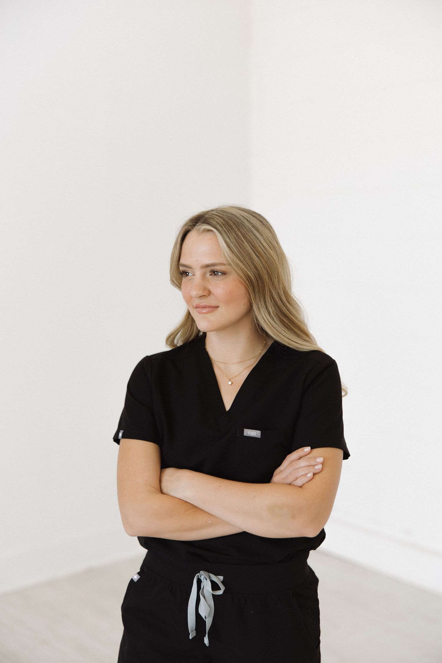 Healthcare worker in black uniform standing with arms crossed in white room.