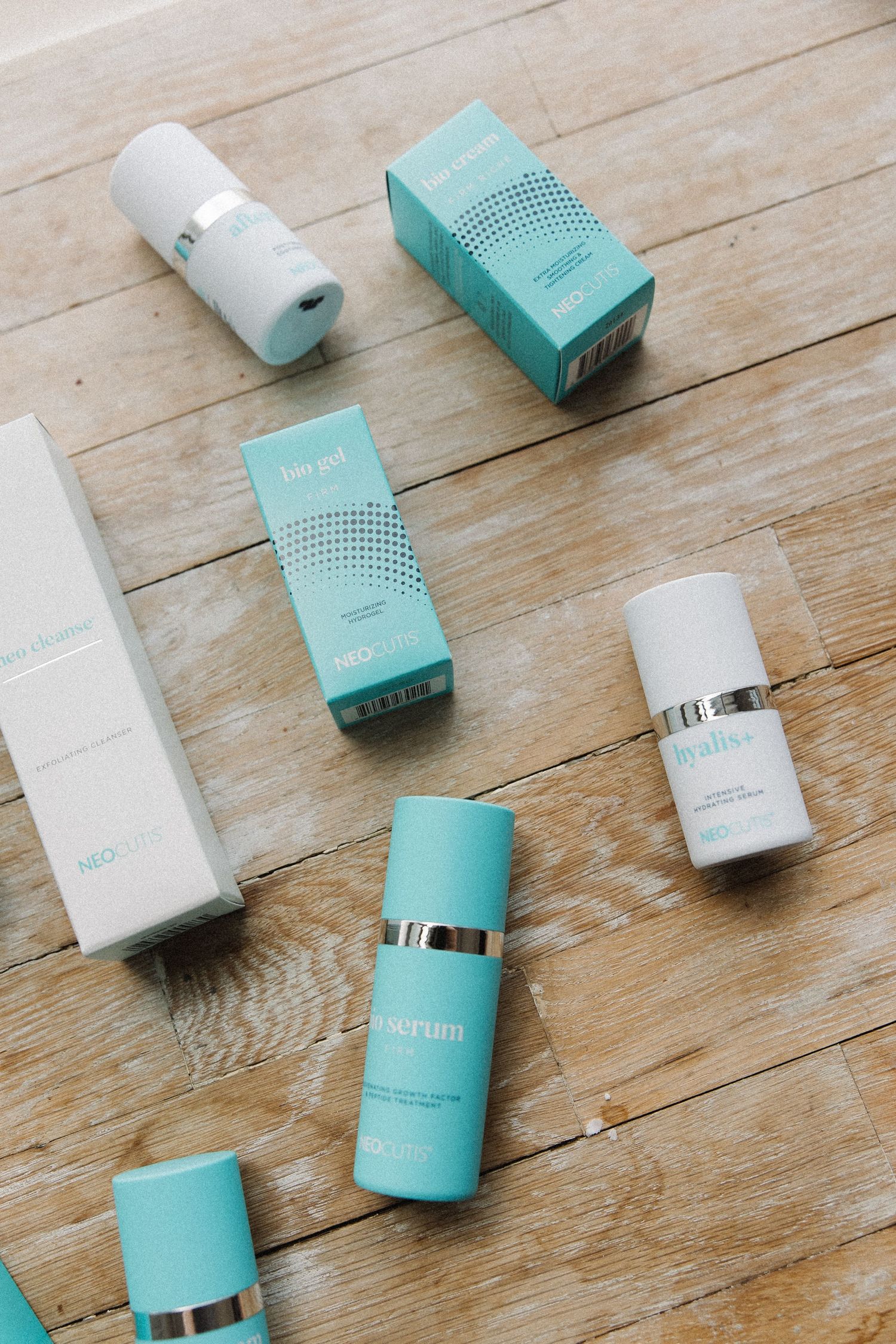 Multiple turquoise and white skincare products and boxes arranged on wooden flooring.