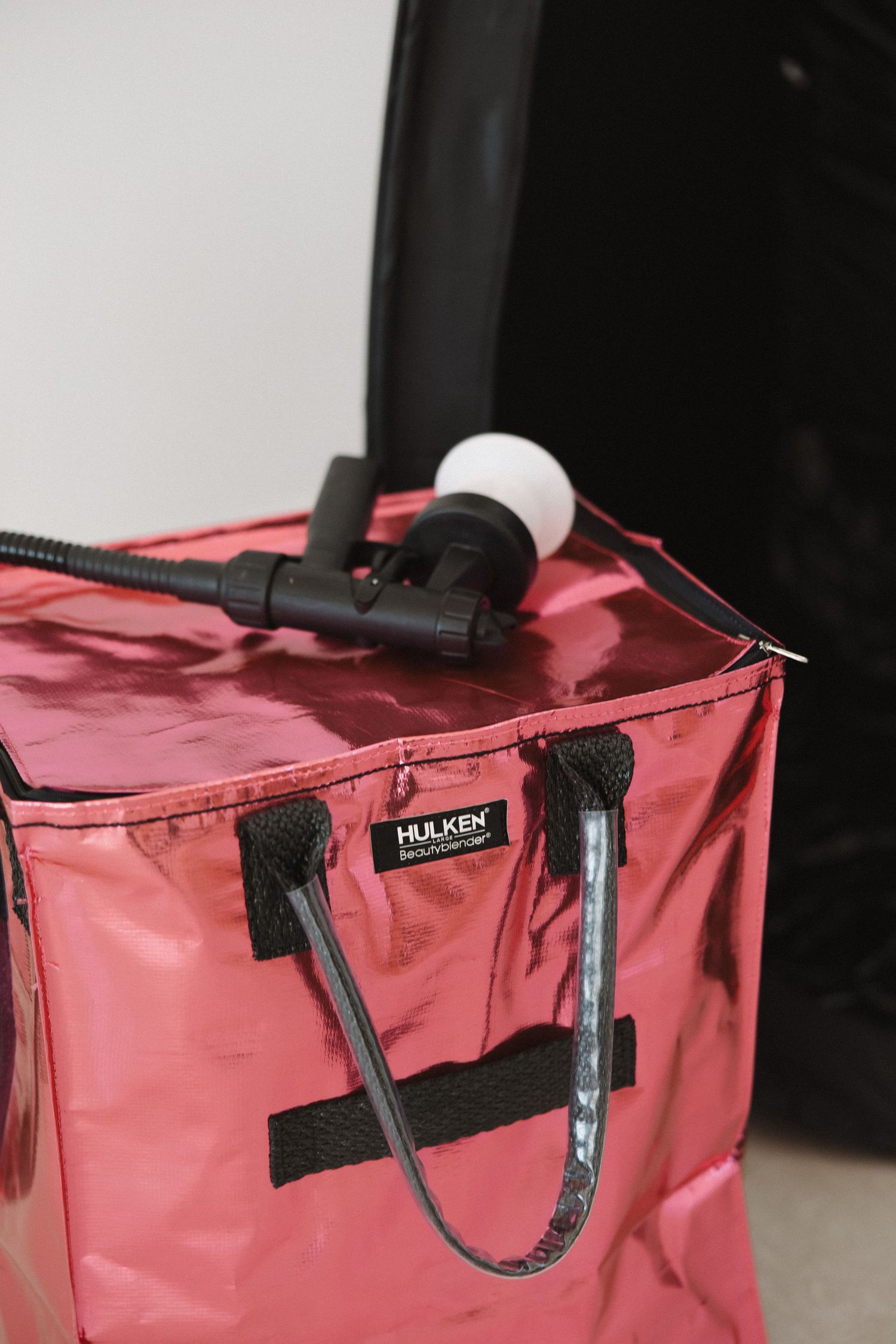 Close-up of pink translucent bag with black straps and spray nozzle attachment.