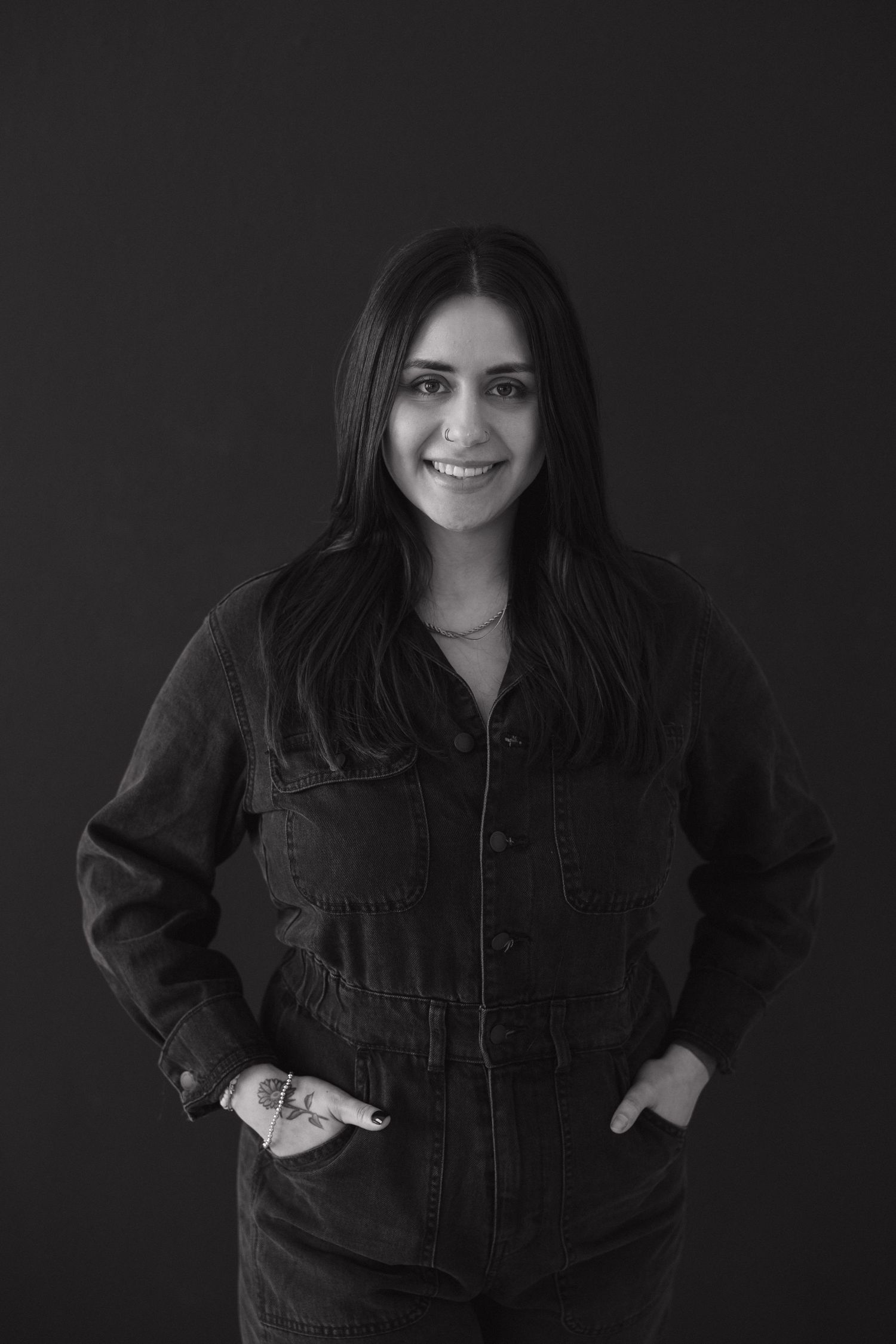 Person wearing black denim jacket poses against dark backdrop in studio setting.