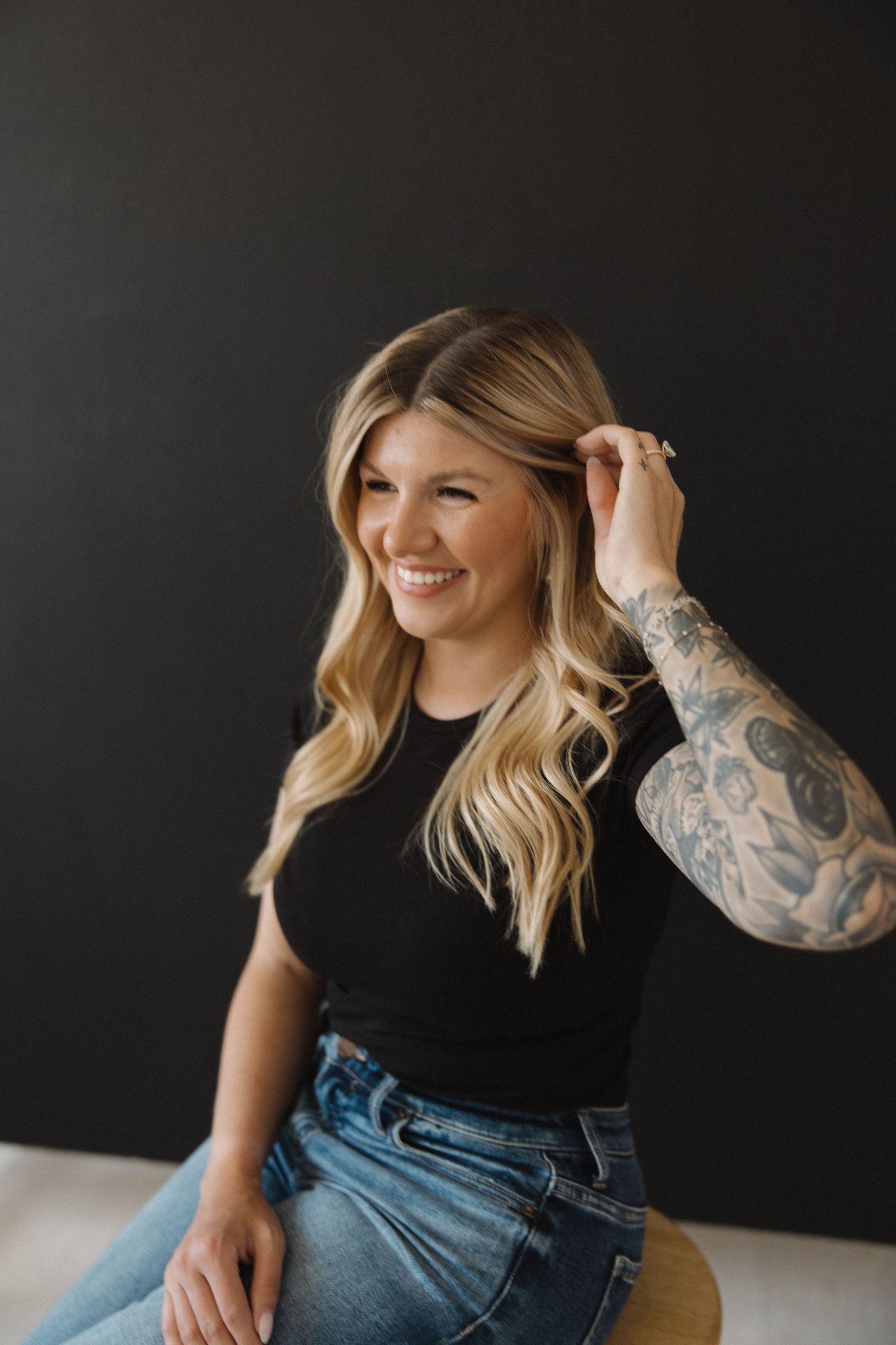 Casual portrait against dark background showing denim and tattoos.