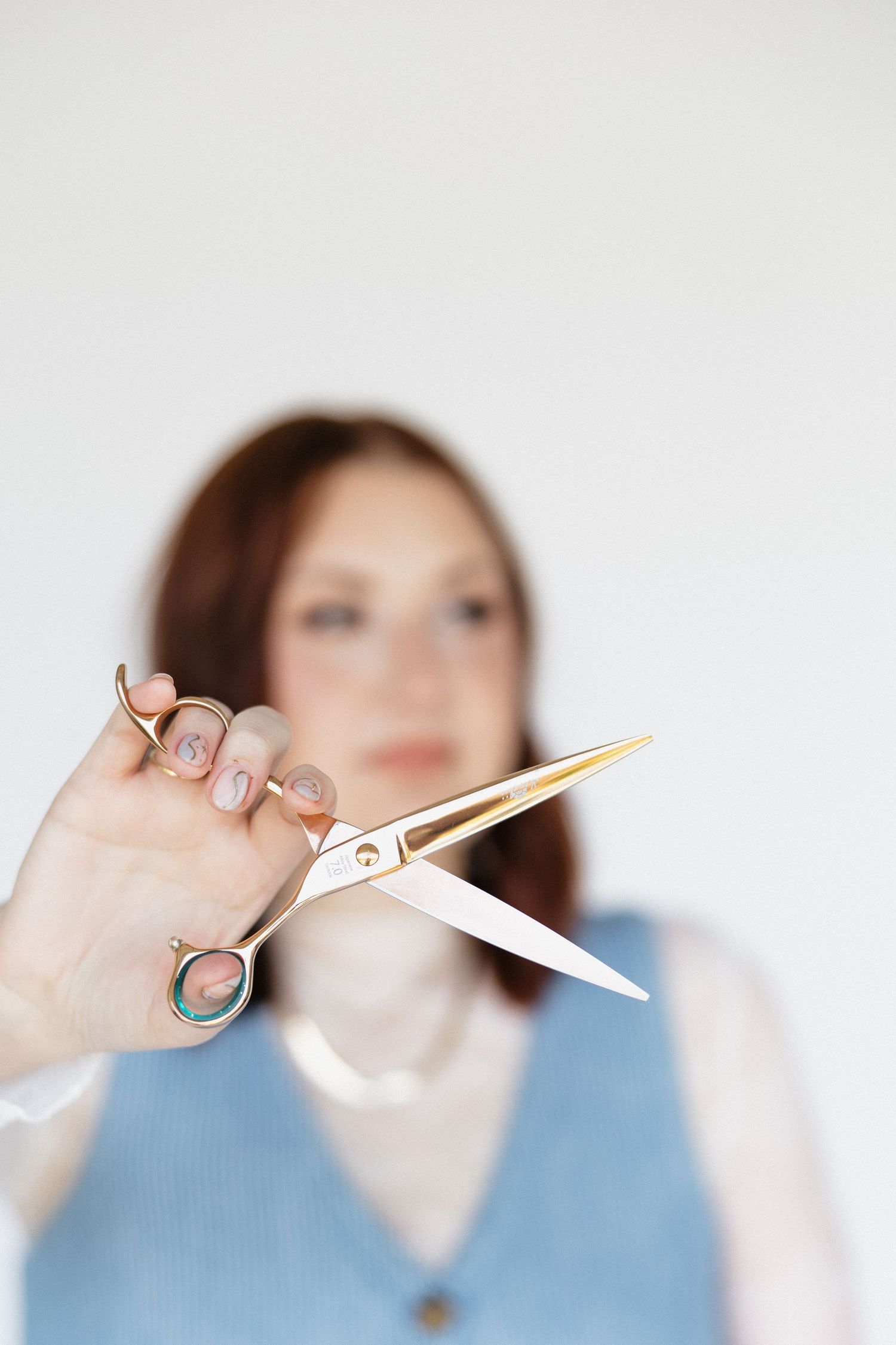 Hands demonstrating cutting motion with gold scissors against white backdrop.