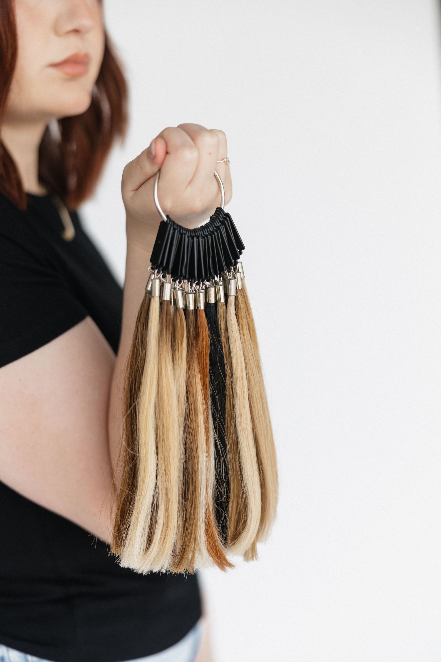 Hand holding blonde and dark hair extension samples on display ring.