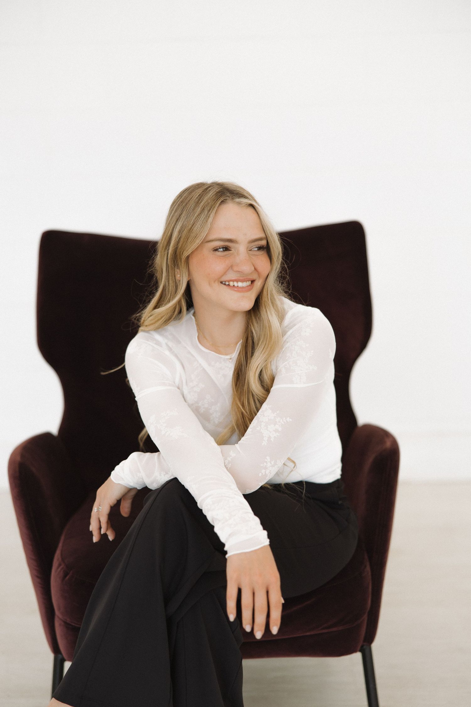Candid studio portraits showing joyful expressions while seated in plush dark armchair.