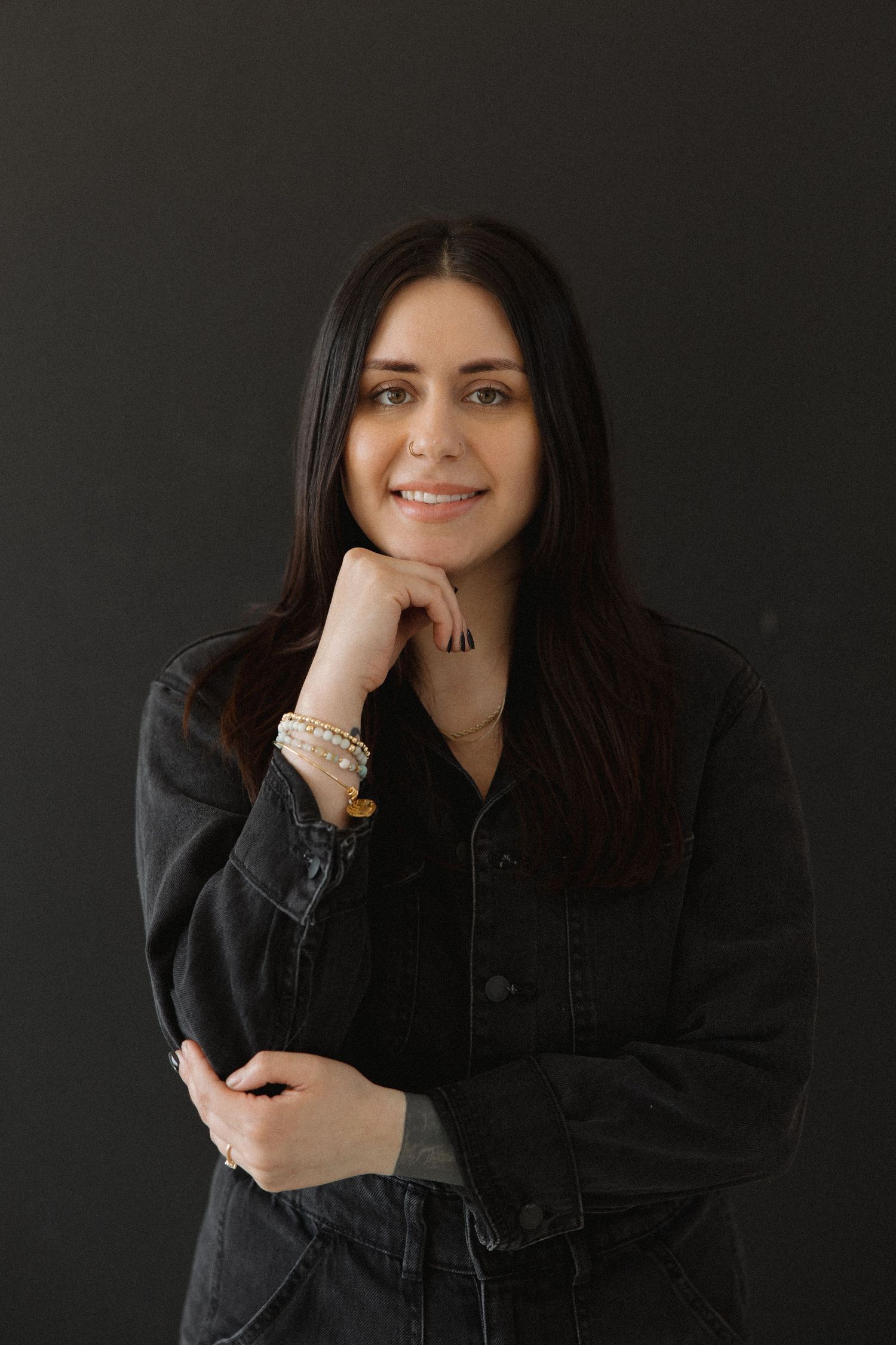 Person in black jacket poses casually against dark backdrop in studio.