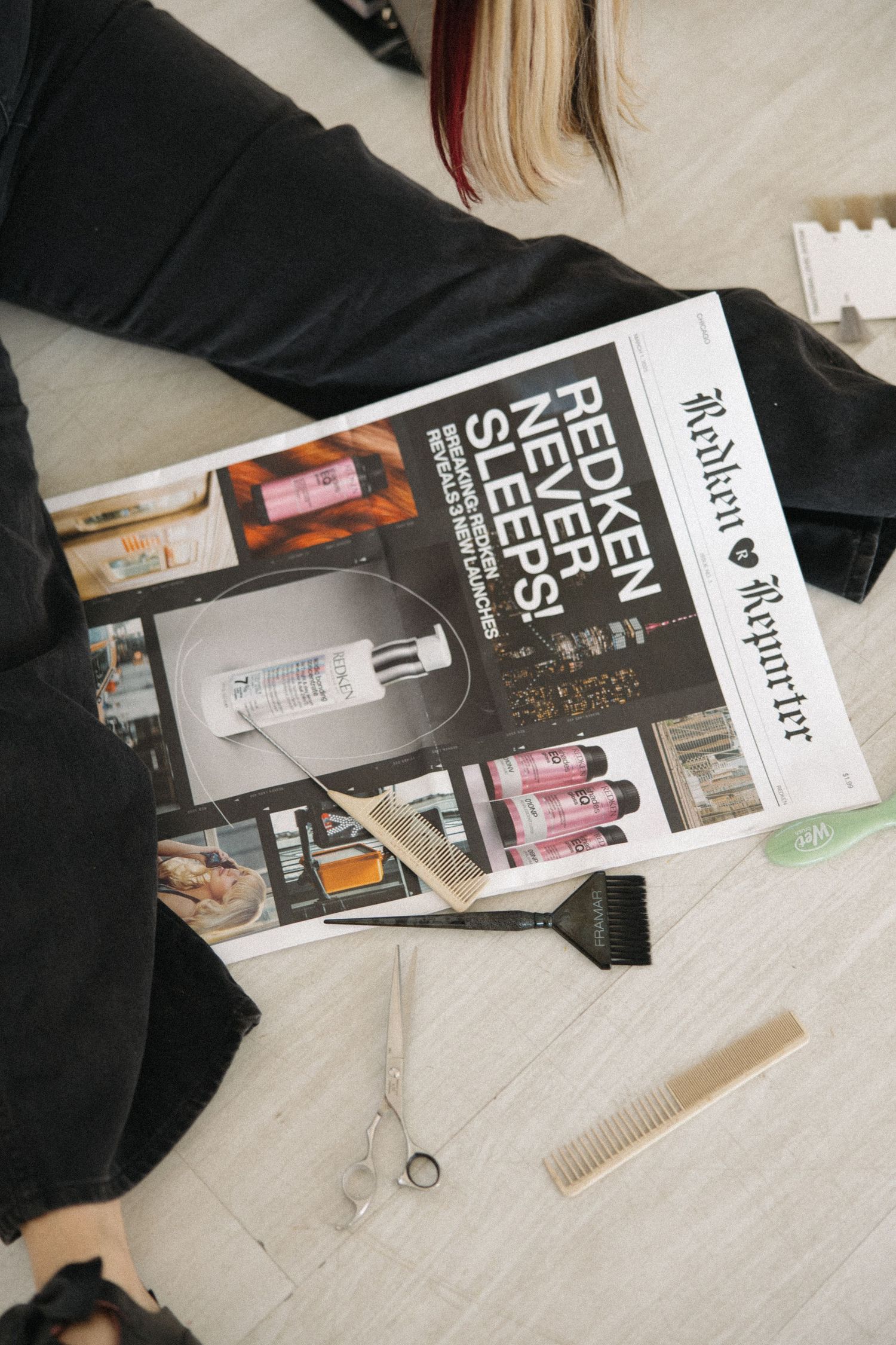 Close-up of fashion magazines and styling tools arranged on wooden floor.