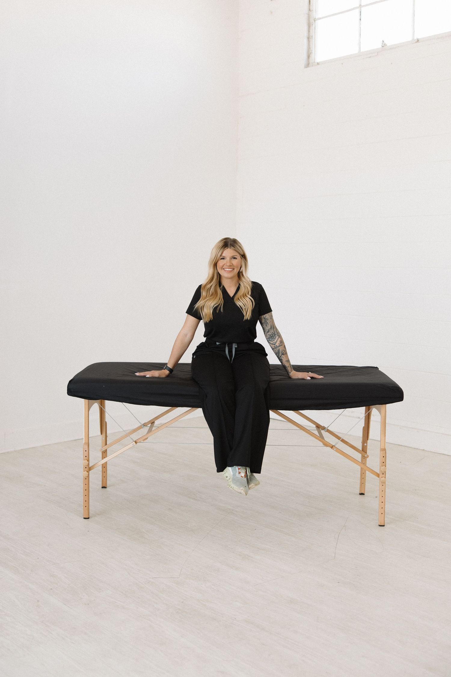 Professional demonstrating poses on black massage table in bright studio setting.