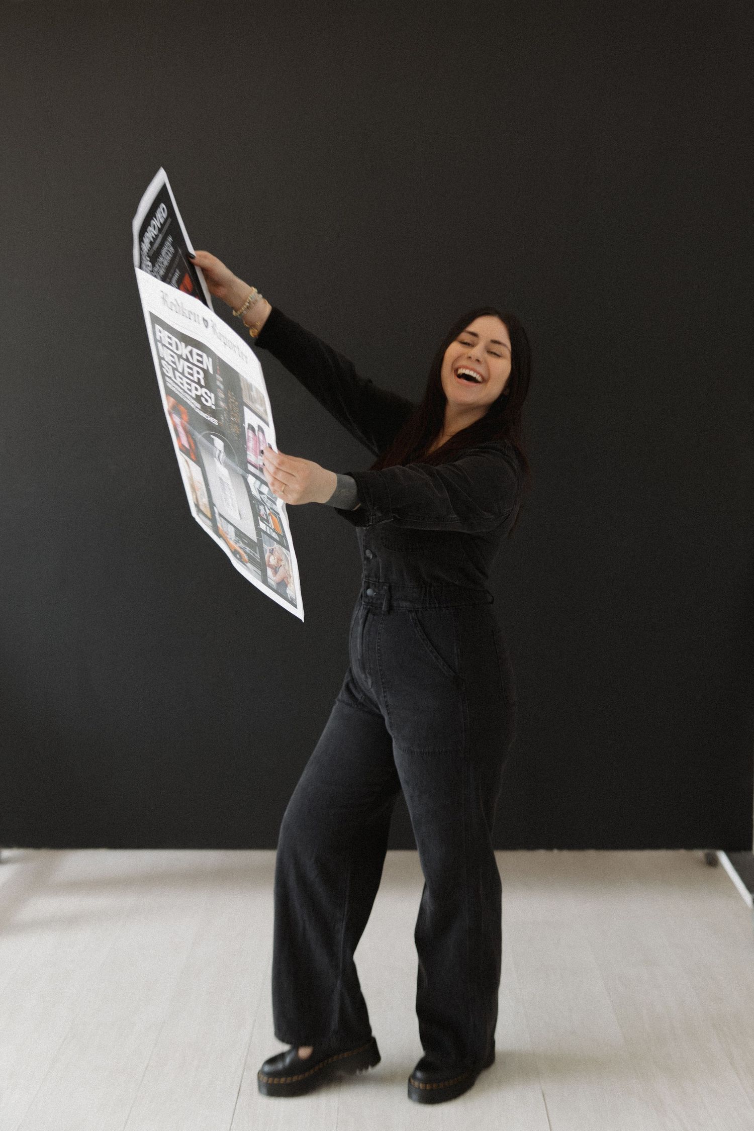 Person in black clothing holds up and reads a promotional brochure against dark background.