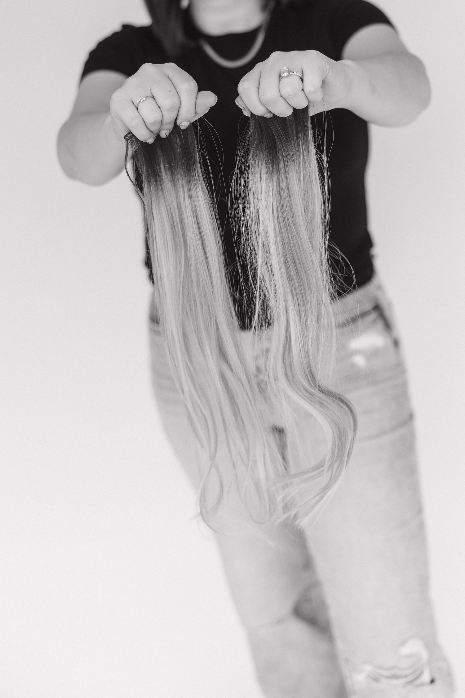 Hands holding blonde hair extensions while wearing light denim jeans.