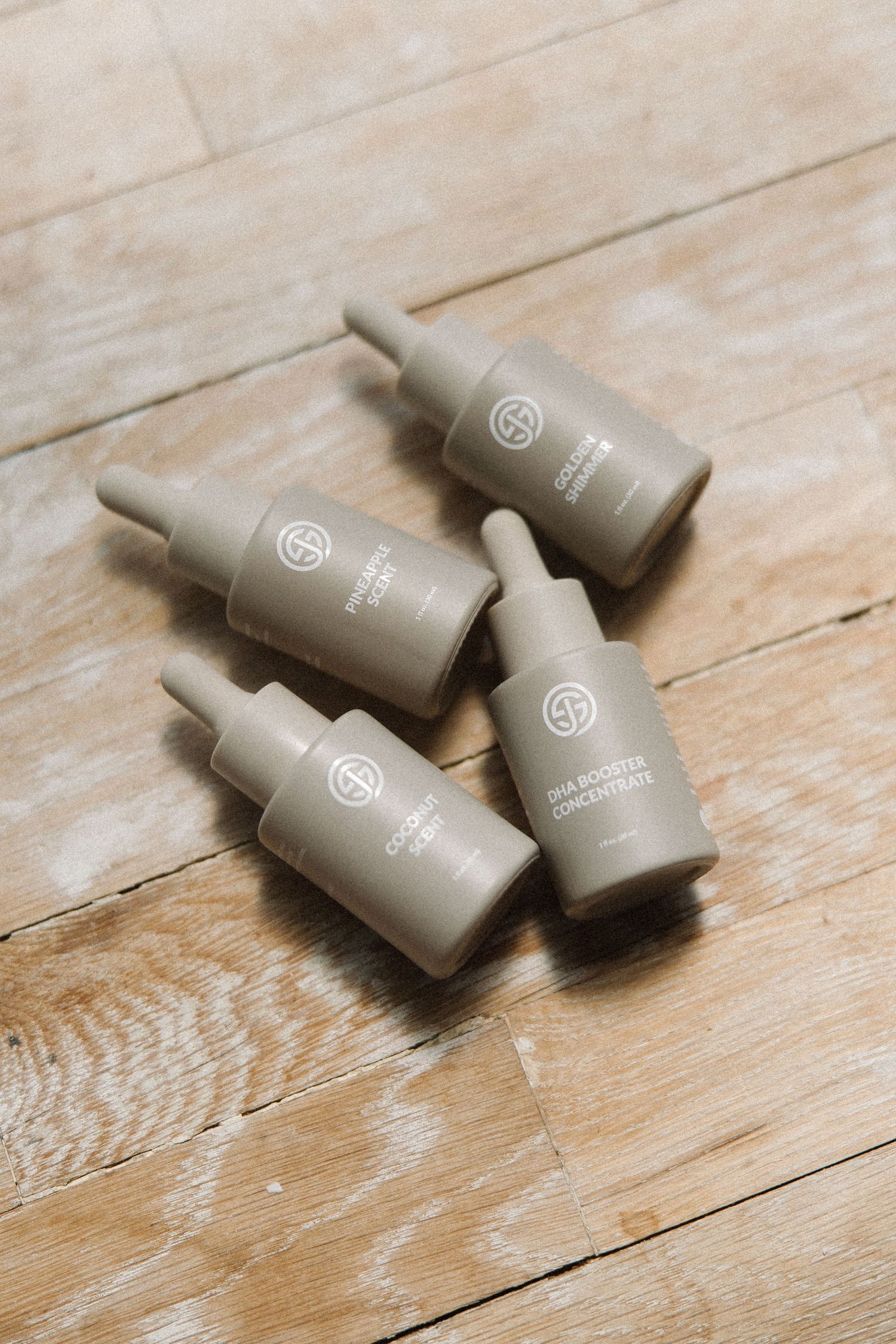 Four small grey cosmetic bottles with dropper caps arranged on a wooden surface.
