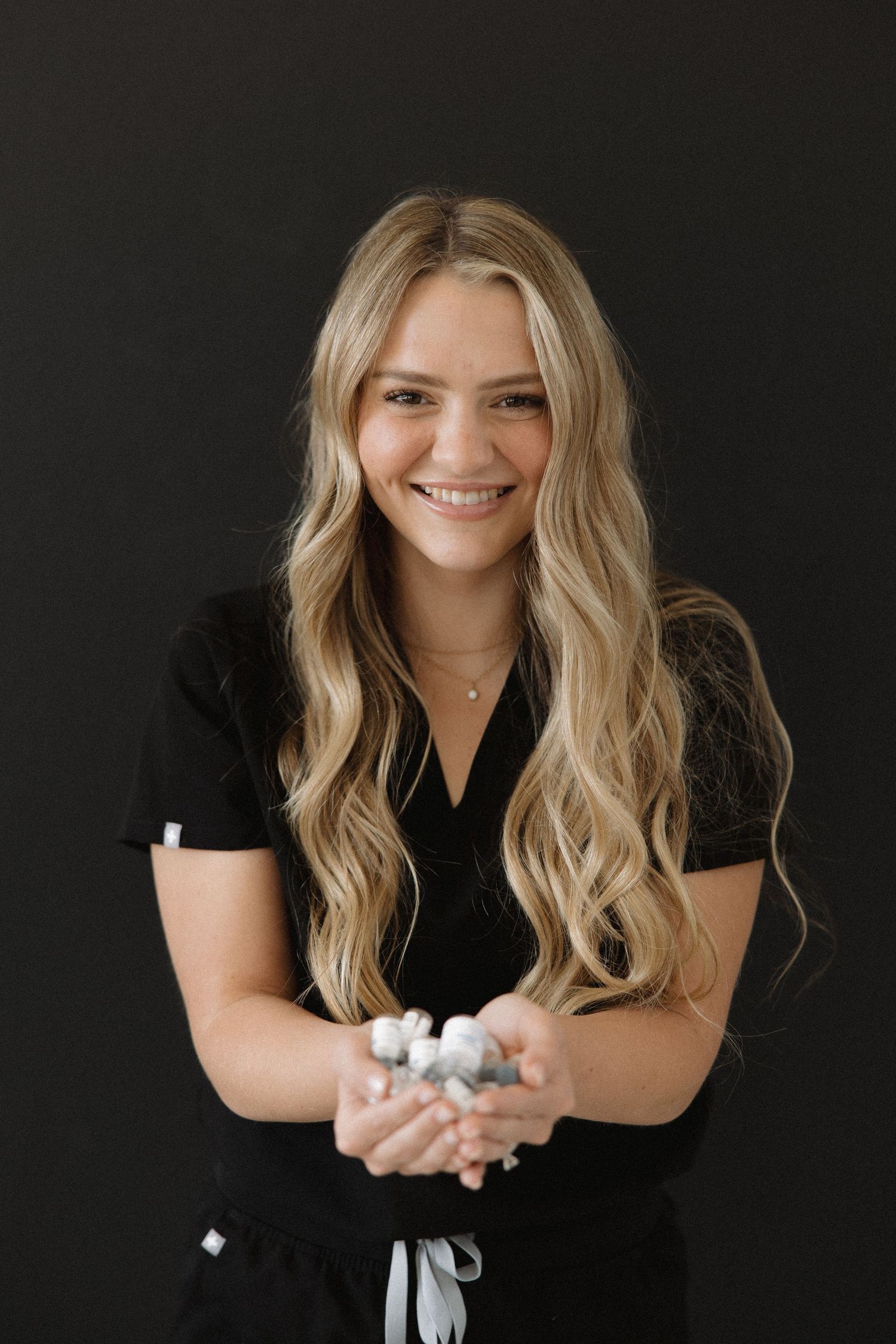 Healthcare provider in black uniform displays medical supplies against dark background.