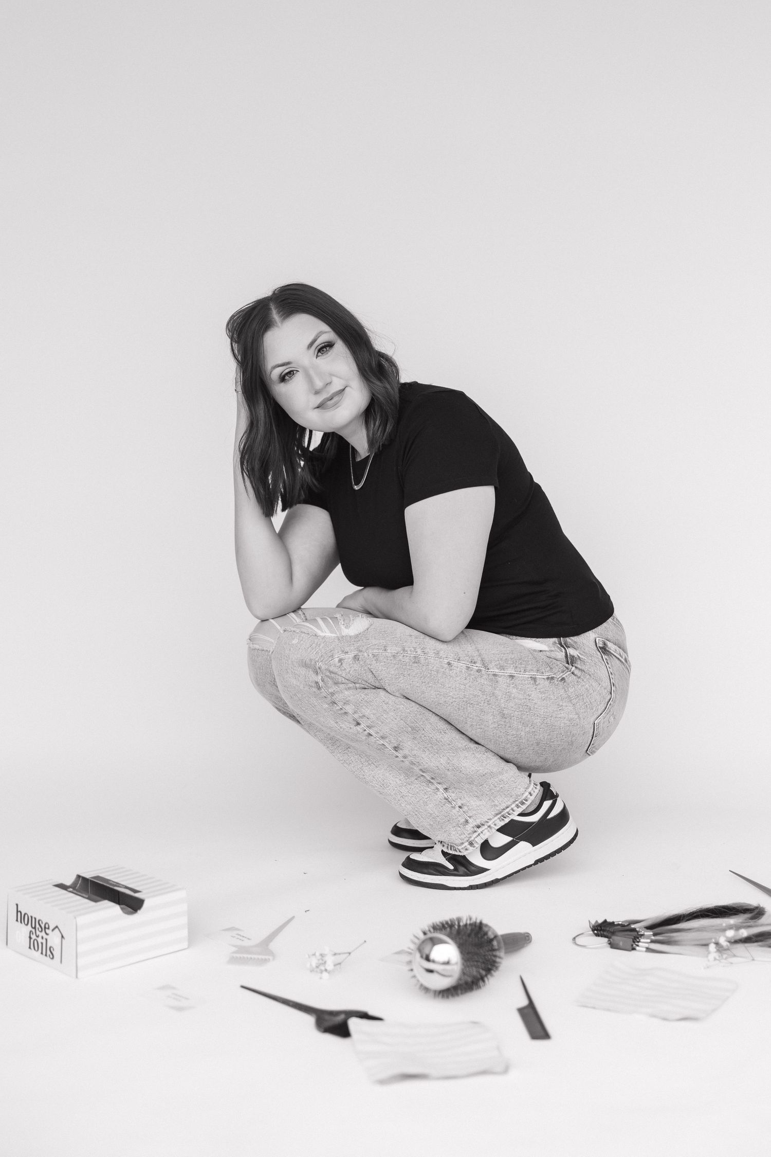 Hair stylist surrounded by professional tools and cards in casual studio setting.