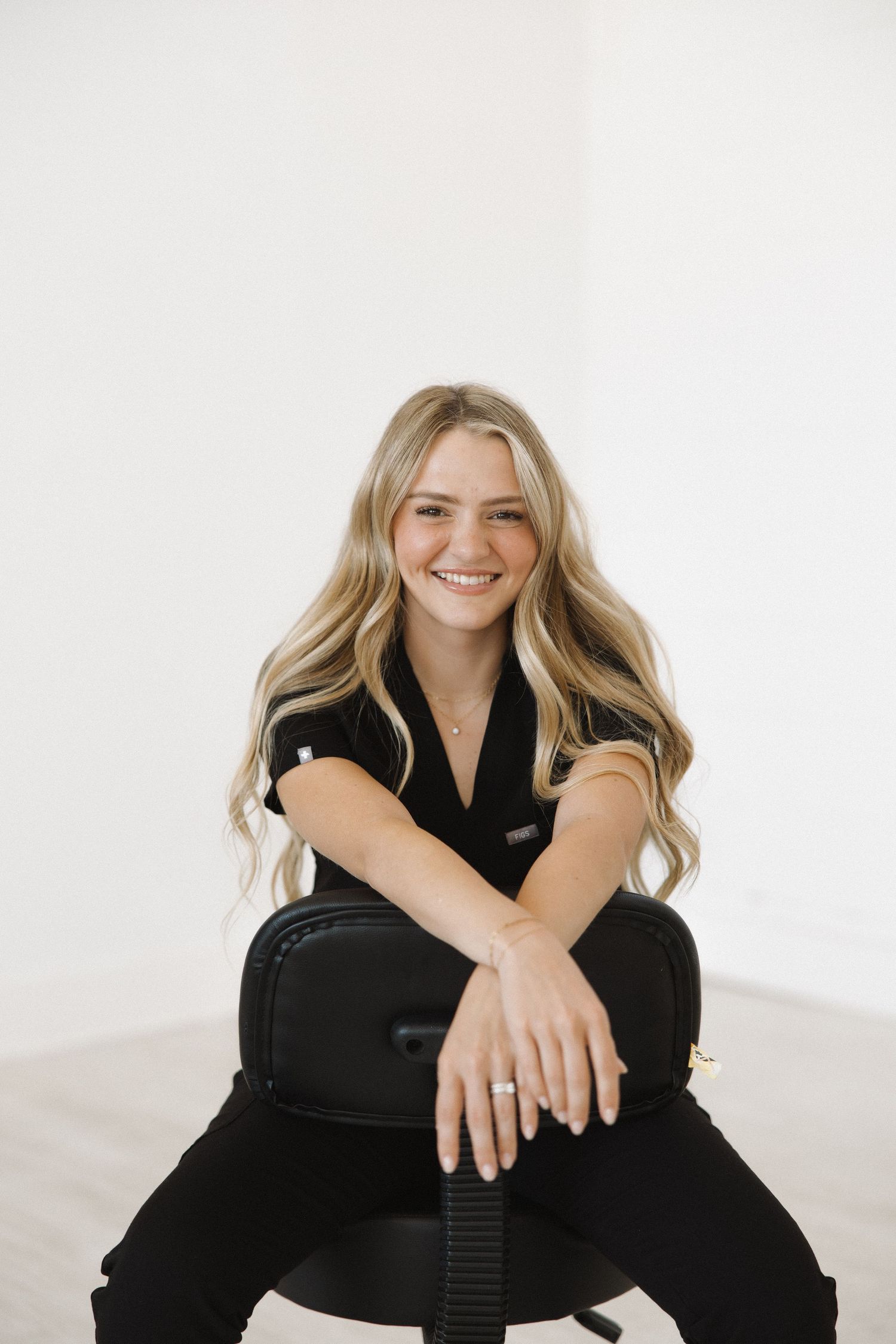 Person in black outfit sitting casually and smiling against white background.