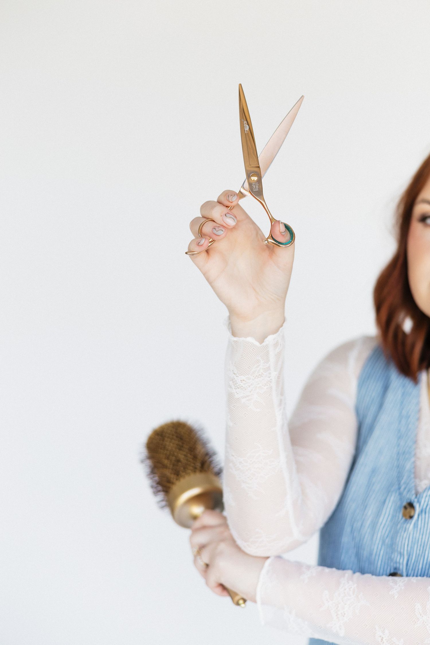 Hands holding gold scissors and hair styling tools against white background.