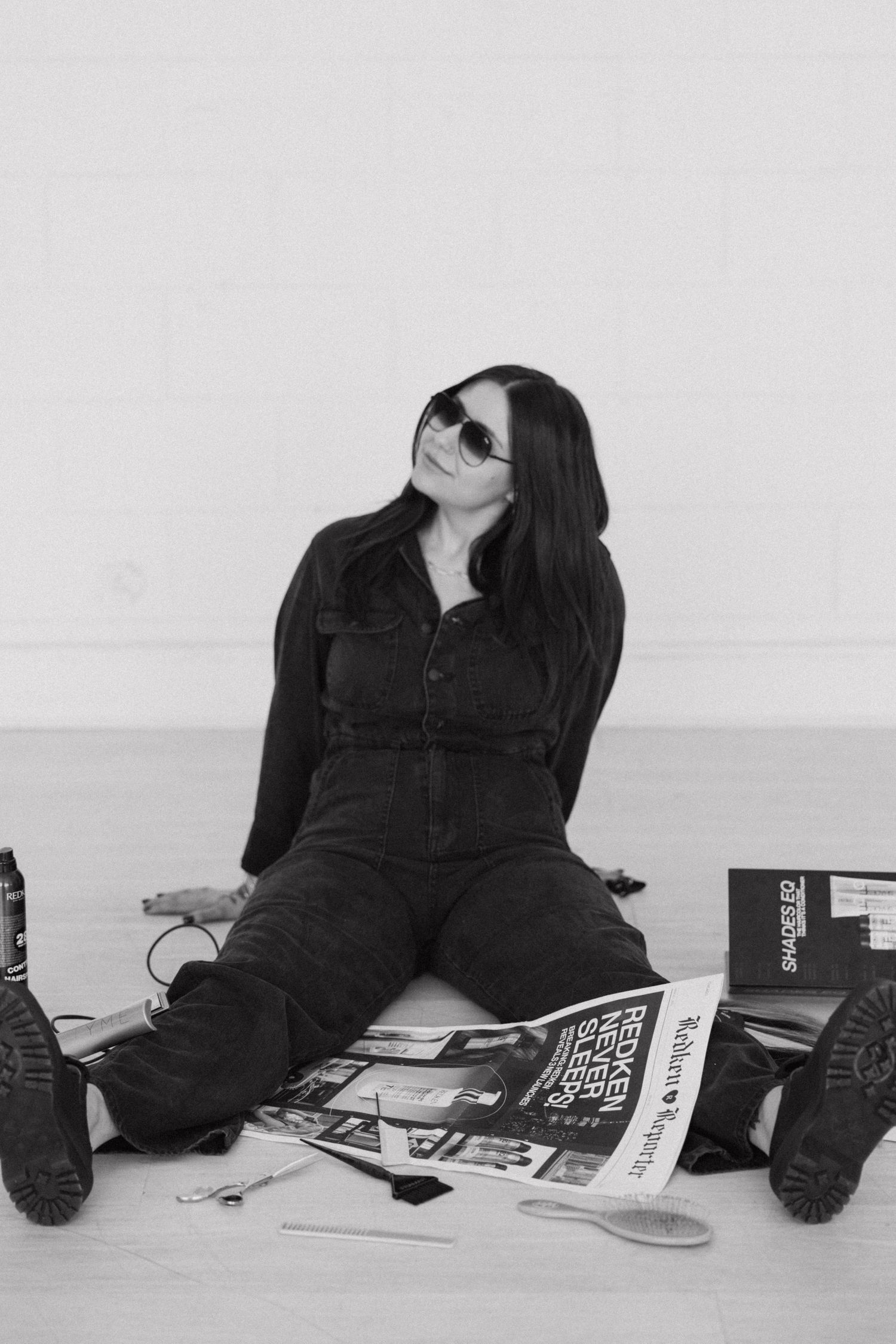 Person in black outfit reclining against white wall with magazines.