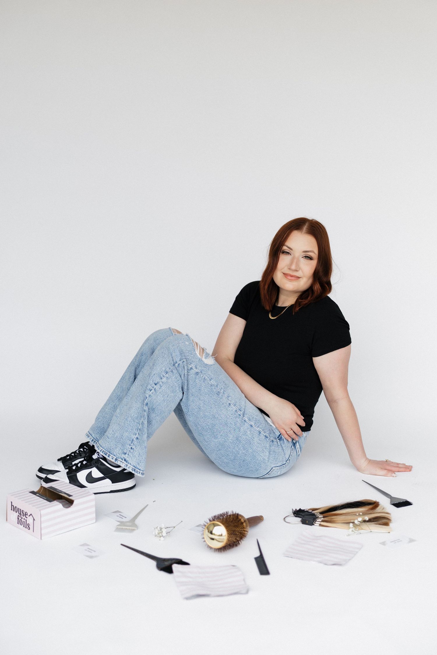 A casual styling setup with hair tools, papers and sneakers arranged on white floor.